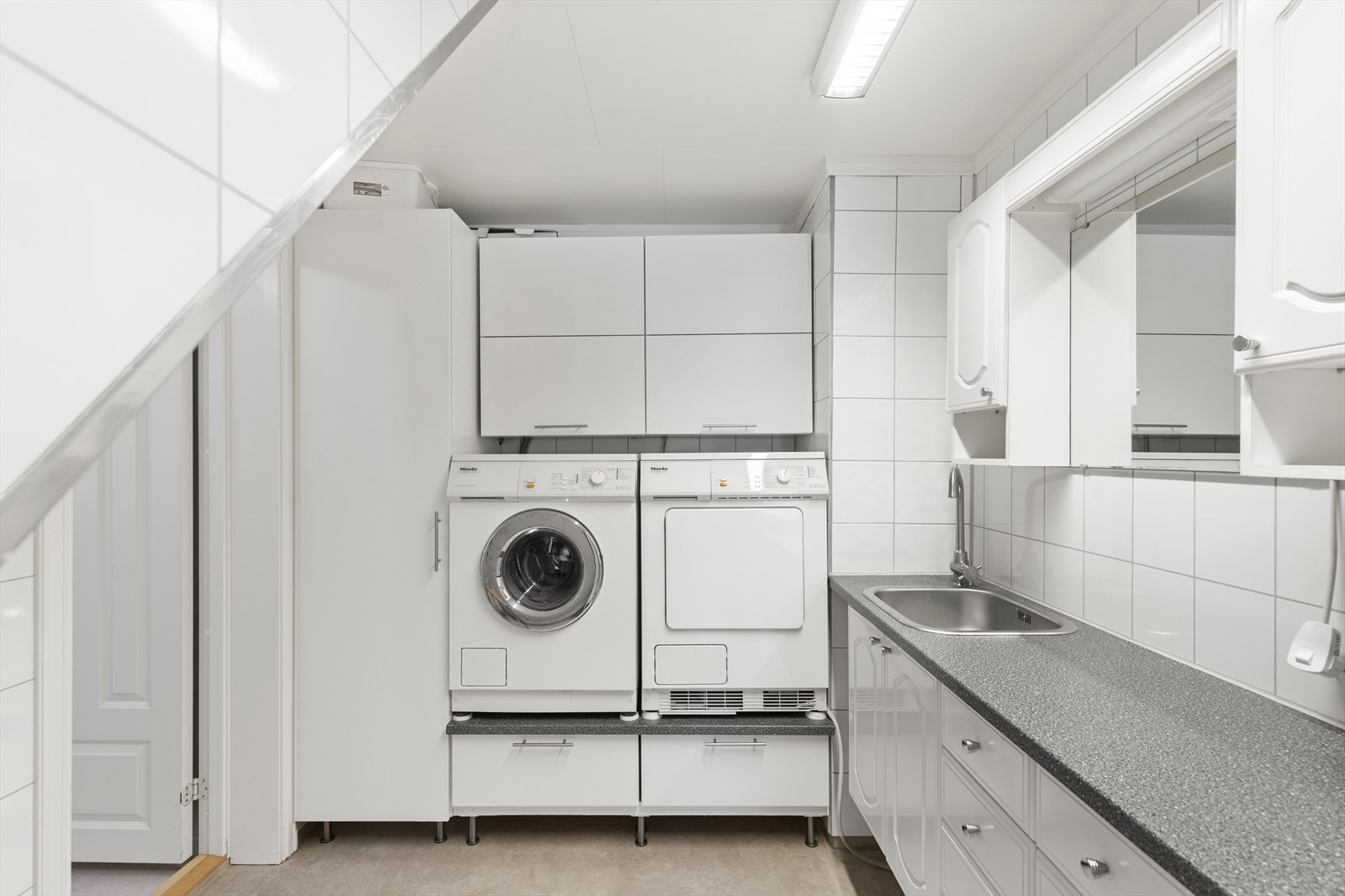 Praktisk vaskerom med skap- og skuffeinnredning, skyllekar og godt med benkeplass til bretting av klær. Galleribilde