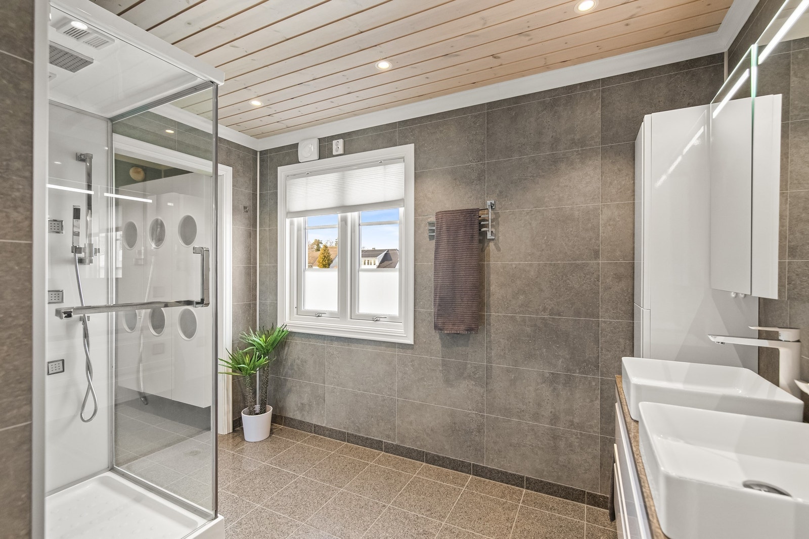 Badet er stort og praktisk innredet med dusjkabinett (massasjedusj), dobbelservant med sideskap og skuffer i innredning samt vegghengt toalett Galleribilde