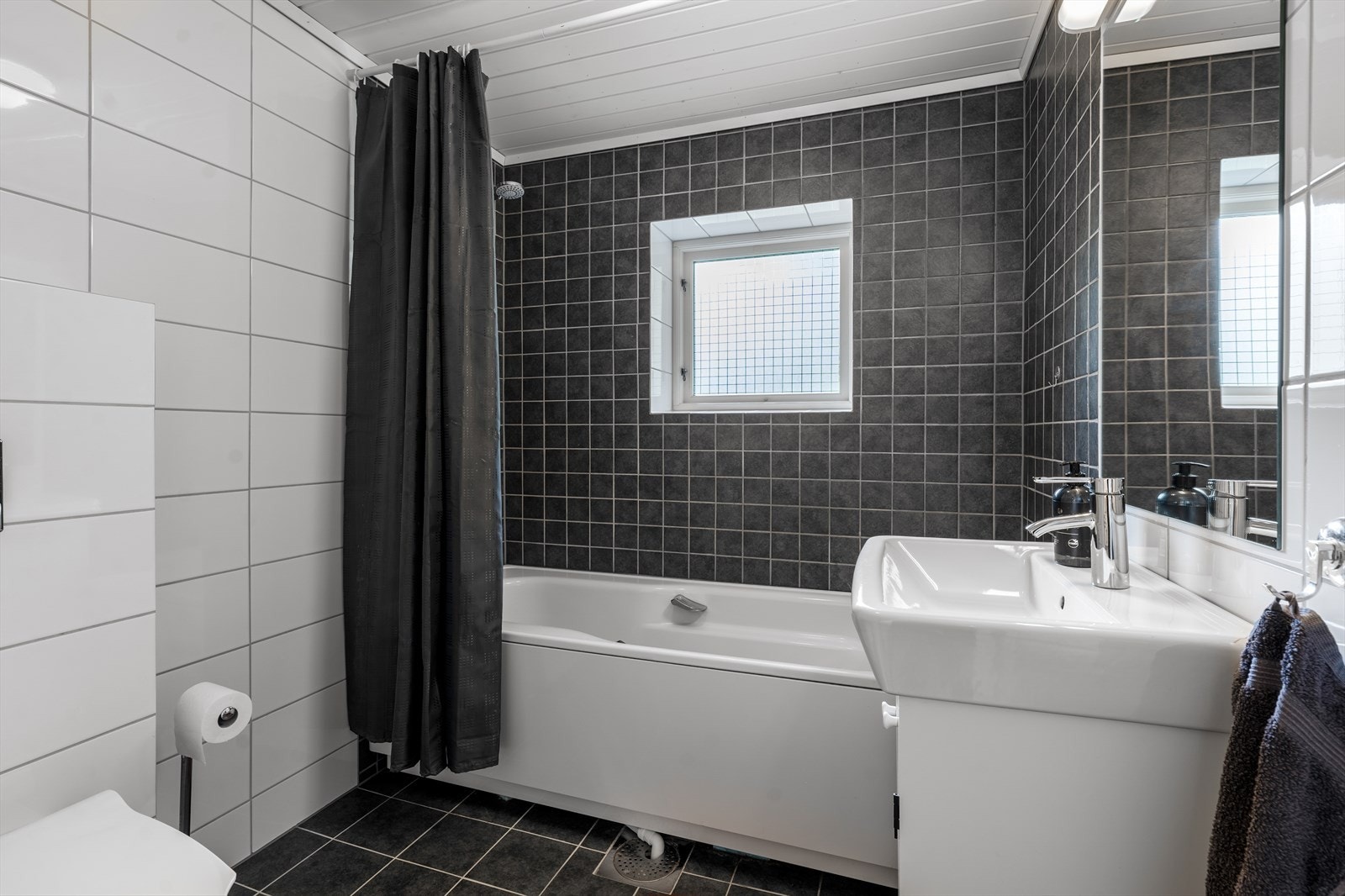 Pent bad fra 2014 med flis på gulv og vegger. Badet har vegghengt toalett, badekar og innredning med heldekkende hvit vask, underskap og speil. Varmekabler og elektrisk avtrekksvifte med tilluft under dørblad. Opplegg for vaskemaskin, men ikke el-kontakt. Galleribilde