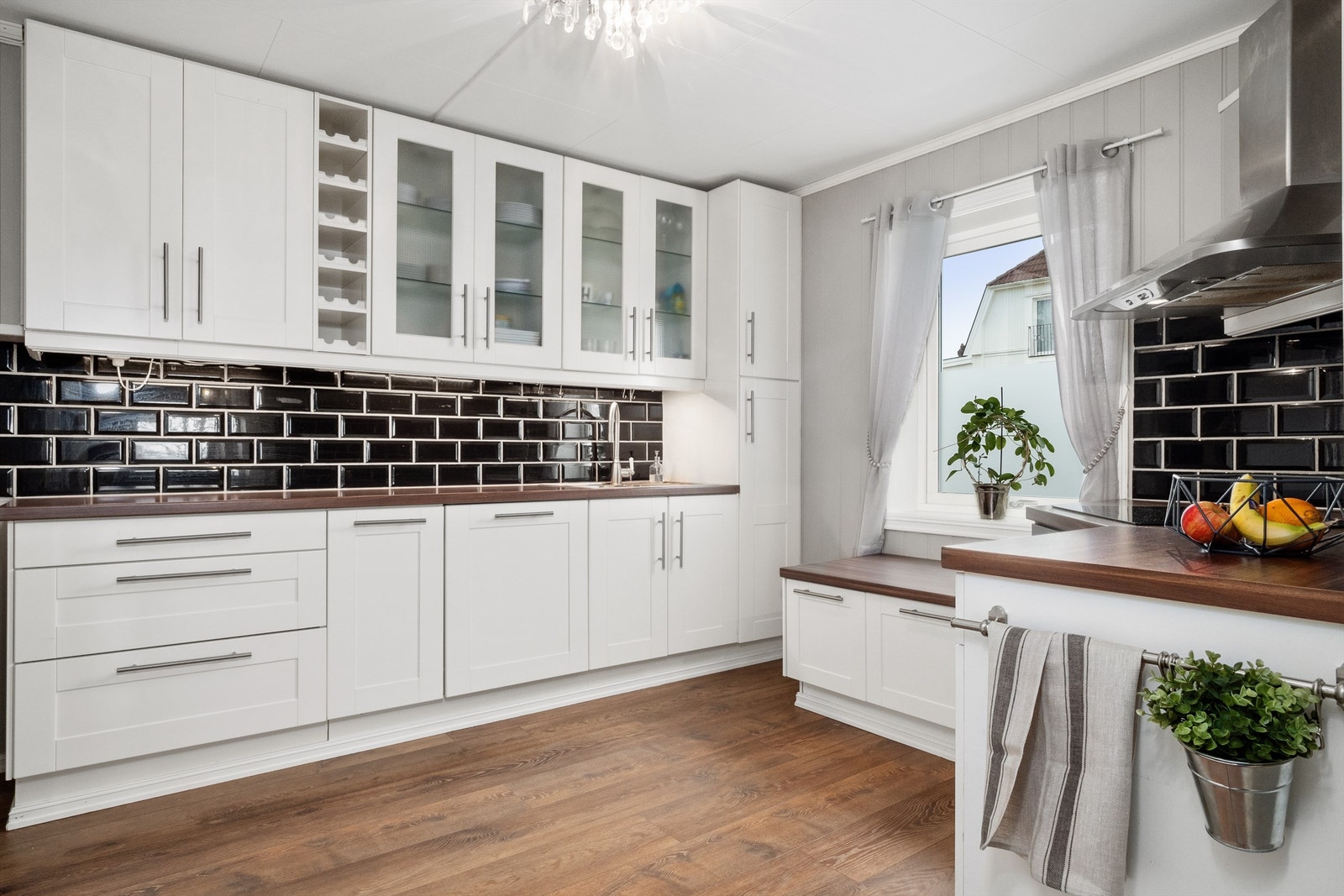 Innholdsrik kjøkkeninnredning fra IKEA med fyllingsfronter, laminerte skrog og benkeplater. Innredningen består av overskap, underskap, skuffer, vinhylle og høyskap. Galleribilde