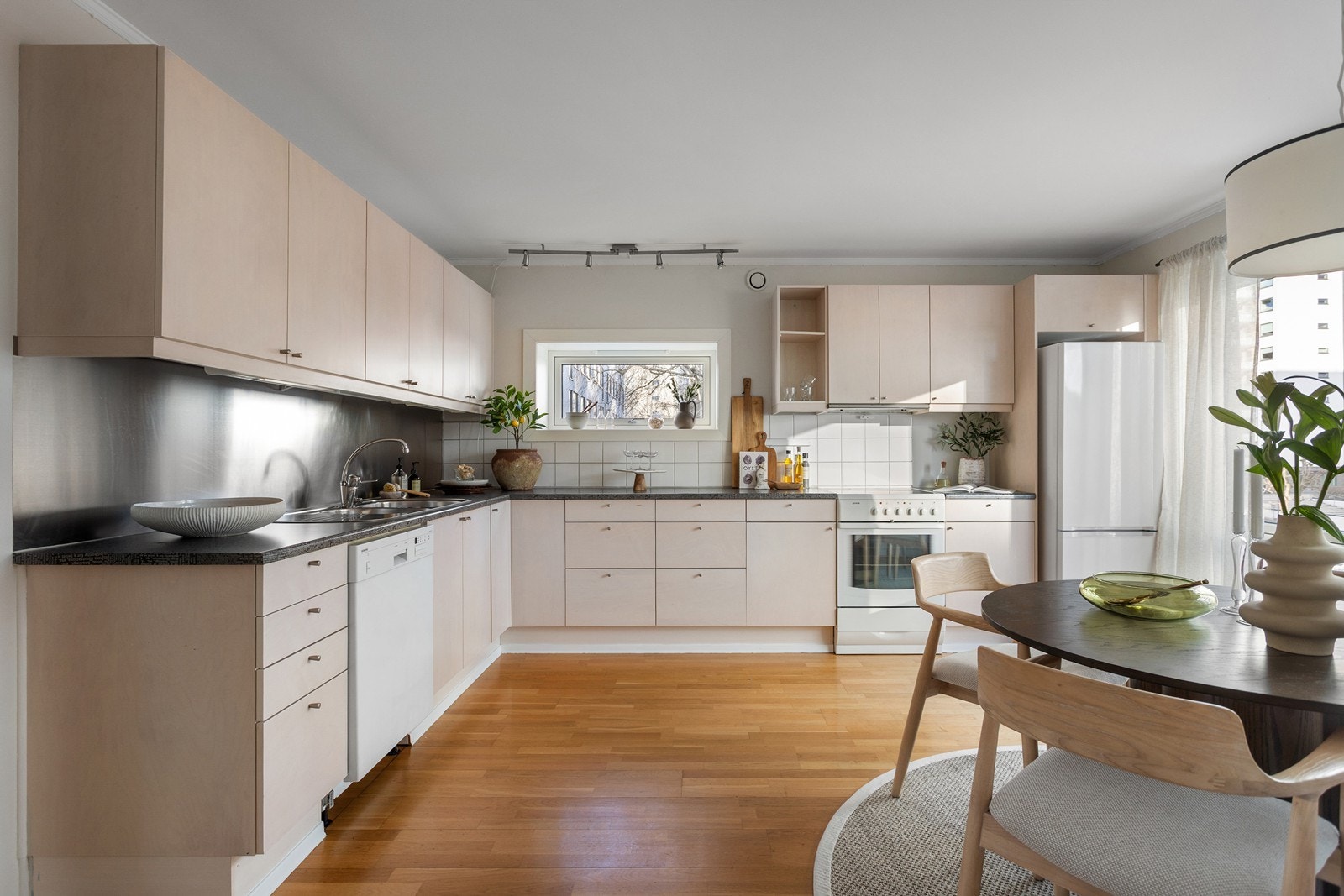 Kjøkkenet har innredning med slette fronter og overskap med benkebelysning. Veggene er delvis dekket med fliser og stålplate. Mørk laminat benkeplate med nedfelt stålkum og ett-greps armatur i krom. Galleribilde