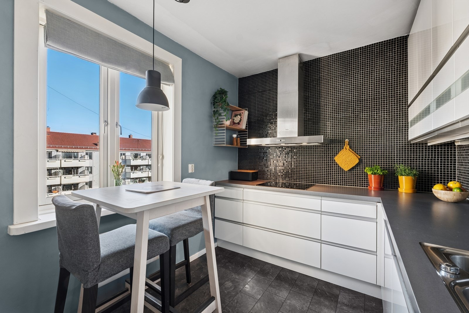 Kjøkkenet er innredet med glatte folierte fronter, laminat
benkeplate med planlimt kum i rustfritt stål og mosaikkfliser på vegg over benk Galleribilde