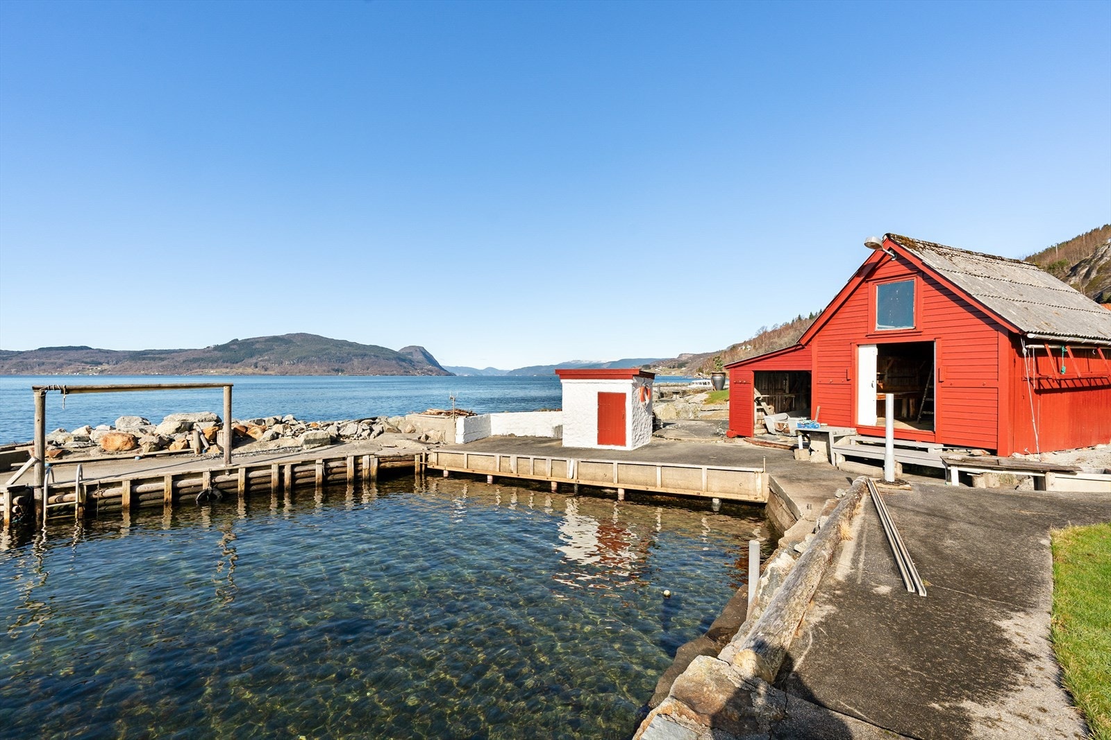 Nydelig eiertomt som er pent opparbeidet med asfaltert innkjørsel, garasje, en stor og flott hage med gressplen, busker og trær, naust med brygge og molo. Galleribilde