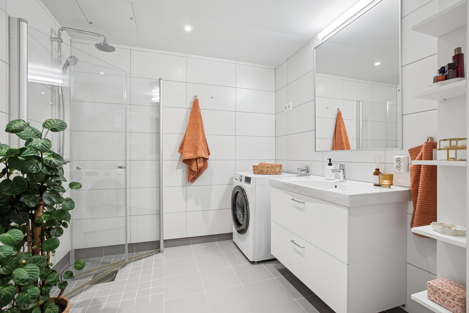 Baderommet er helfliset og har en stilren innredning med hvit servantseksjon, skuffer, dusjlinje med glassdører, vegghengt toalett og opplegg for vaskemaskin. Galleribilde