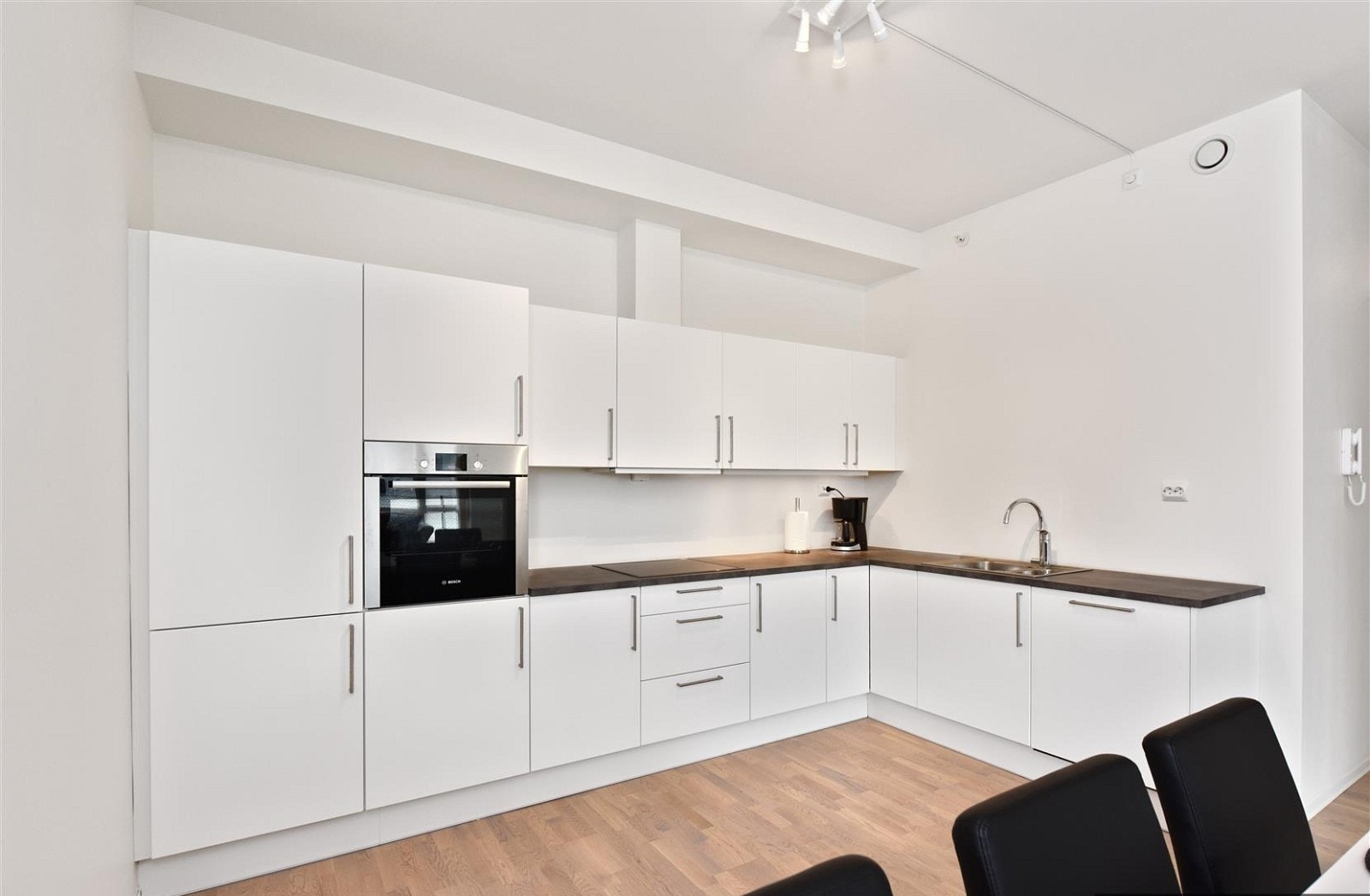 Kjøkken i L-løsning med hvite slette fronter, laminert benkeplate og integrerte hvitevarer. Galleribilde