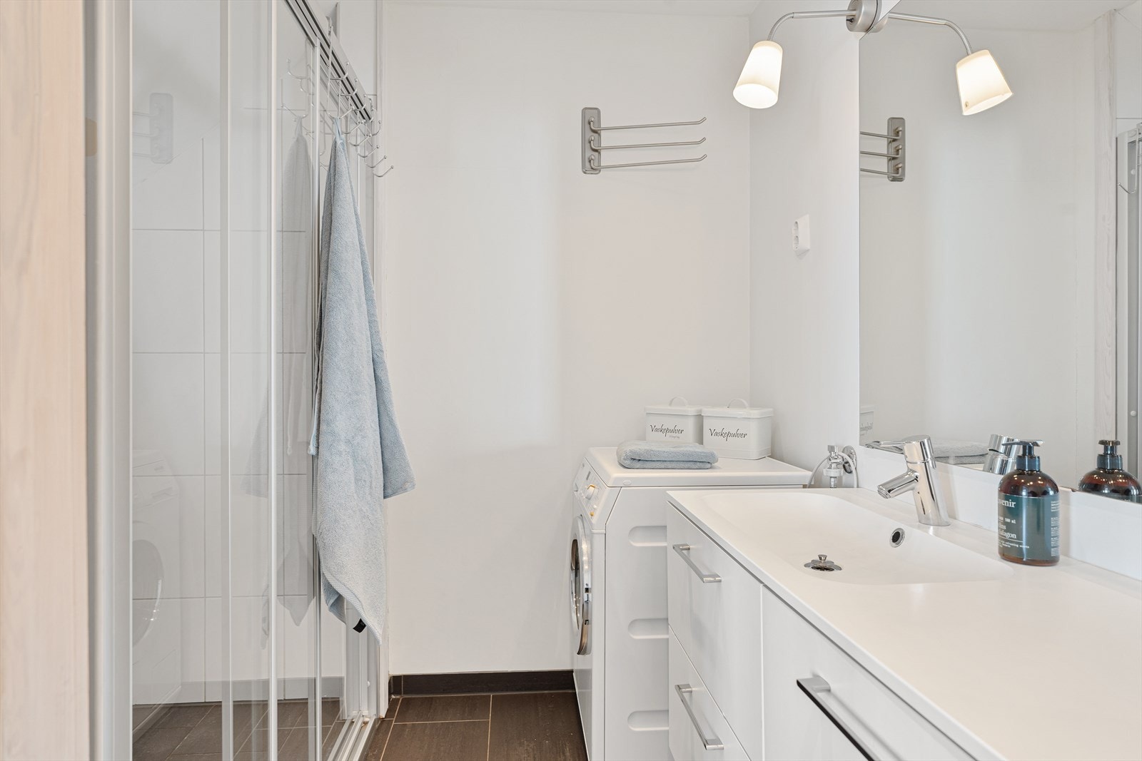 Badet inneholder dusjnisje, opplegg for vaskemaskin, vegghengt toalett og innredning med god oppbevaringsplass Galleribilde