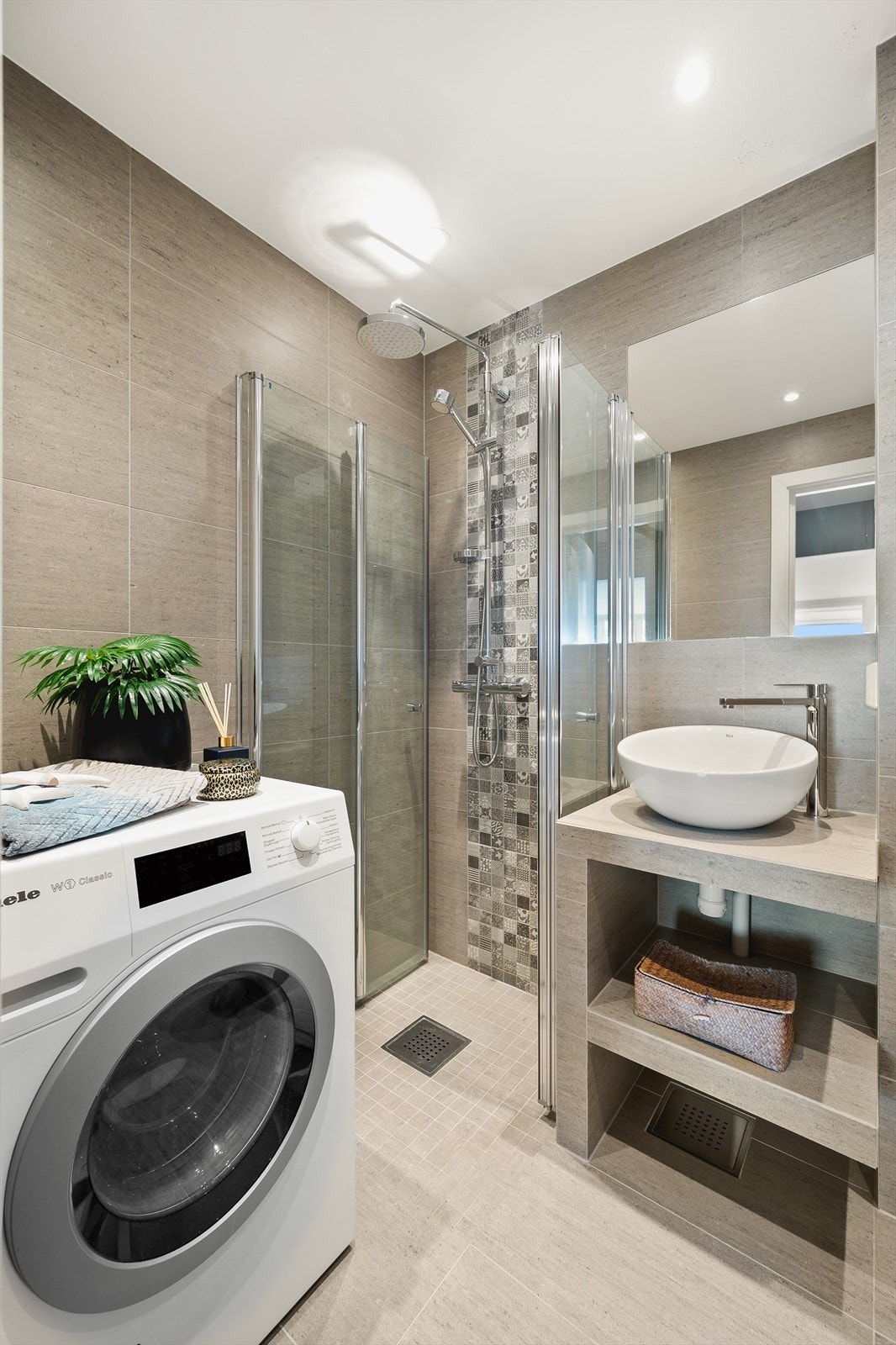 Badet er innredet med vegghengt toalett, servant på innredning og dusjhjørne med svingbare glassdører. Det er opplegg for vaskemaskin. Galleribilde