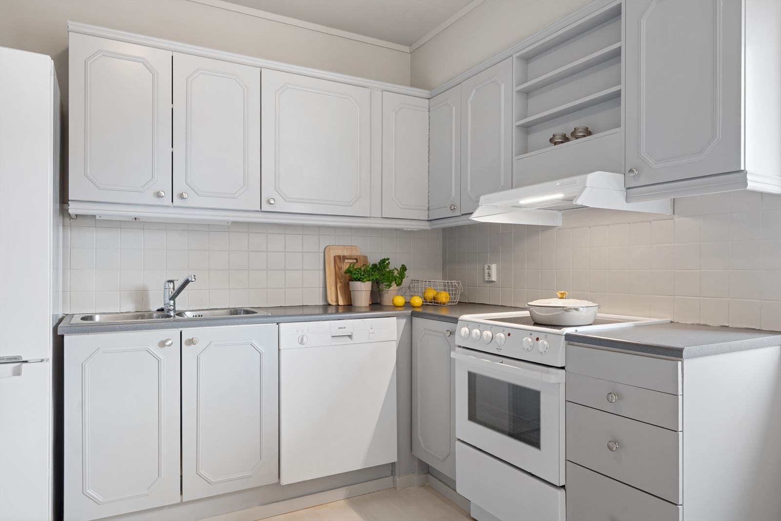 Innredningen har en praktisk vinkelform med malte fronter og fliser, benkeplate i laminat og hvitevarer som medfølger. Galleribilde