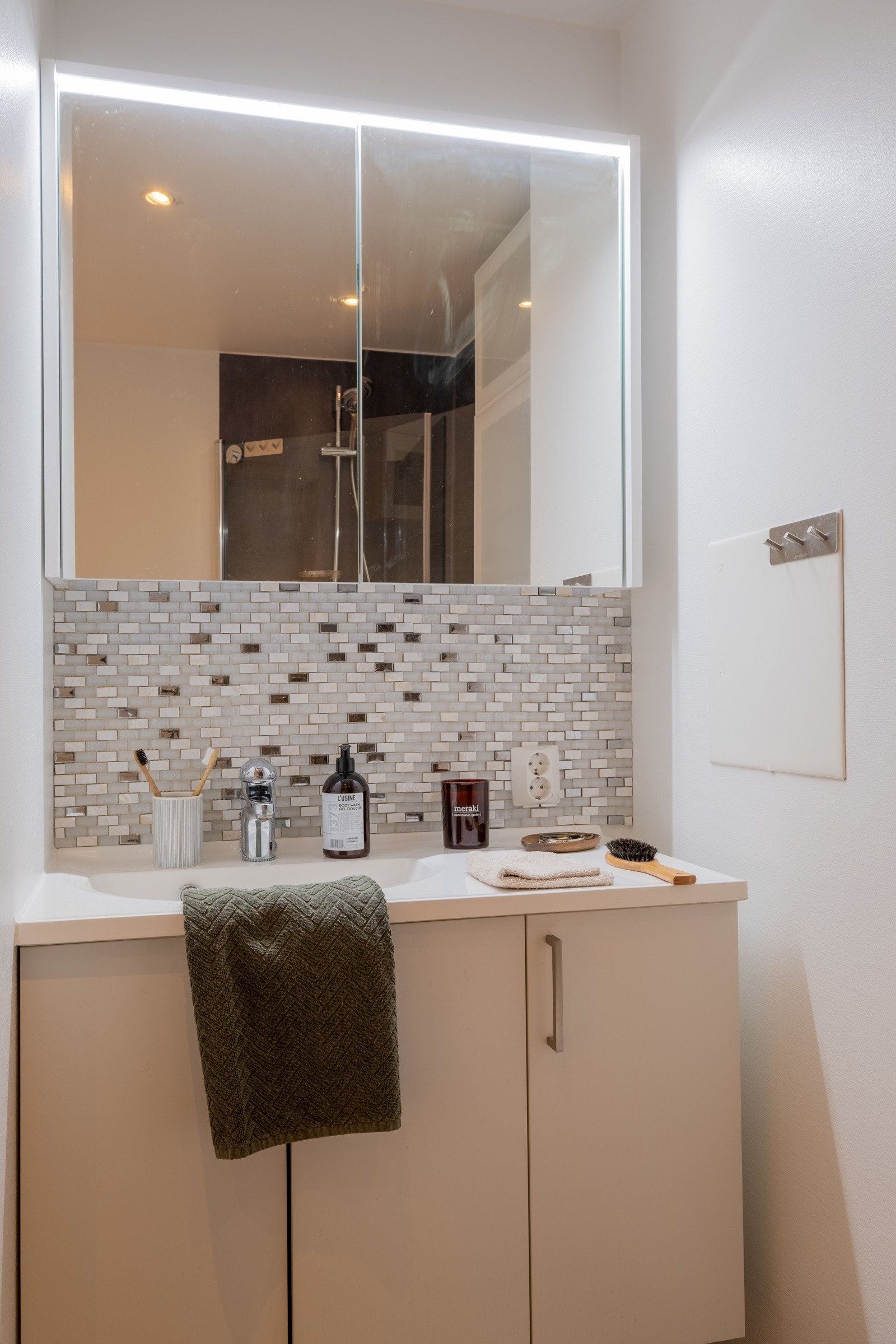 Badet er innredet med dusj med glassdører, vegghengt dusjtoalett, seksjon med vask og skap for oppbevaring og speilskap Galleribilde