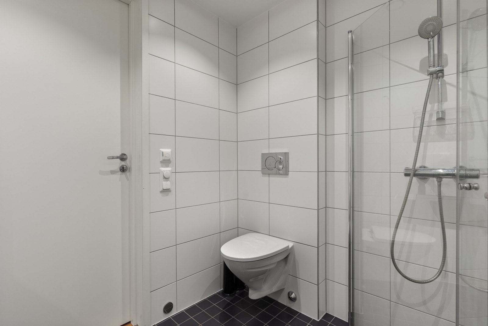 Videre så er det dusjhjørne med innfellbare glassdører og dusjarmatur tilkoblet hånddusj, vegghengt toalett med innebygget sisternekasse og opplegg for vaskemaskin. Galleribilde