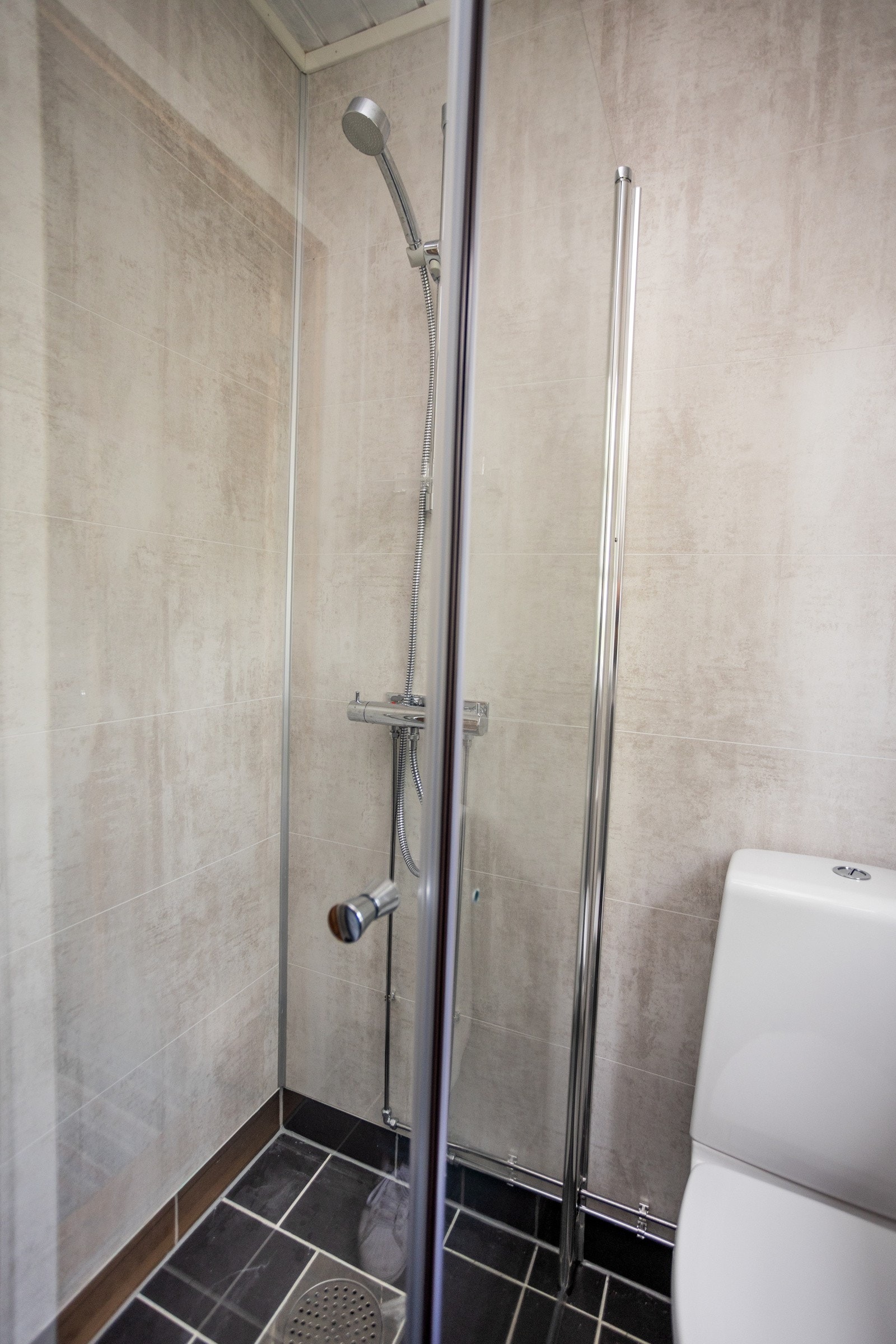 Stilren innredning med vegghengt servant, speilskap, dusjhjørne med dører og gulvstående toalett Galleribilde