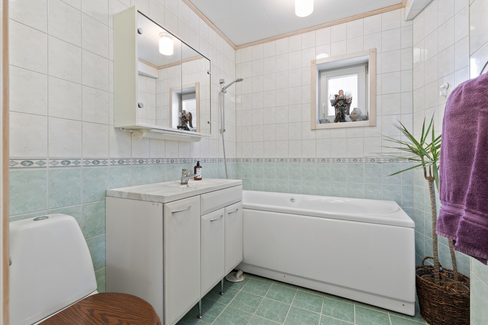 Flislagt bad med standard fra byggeår. Innredningen består av profilert servantmøblement, speilskap, frittstående badekar m/dusjløsning og toalett. Det er lagt varmekabler i gulv. Galleribilde