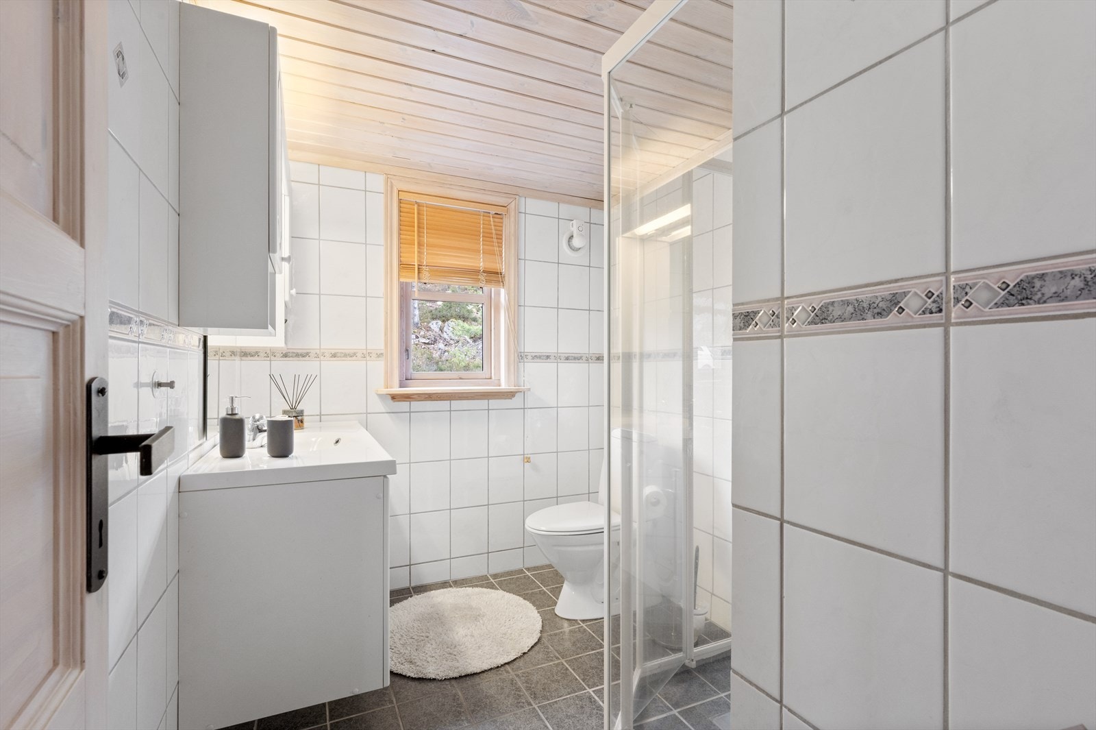 Pent flislagt bad med dusj, helstøpt servant i baderomsinnredning og toalett. Galleribilde