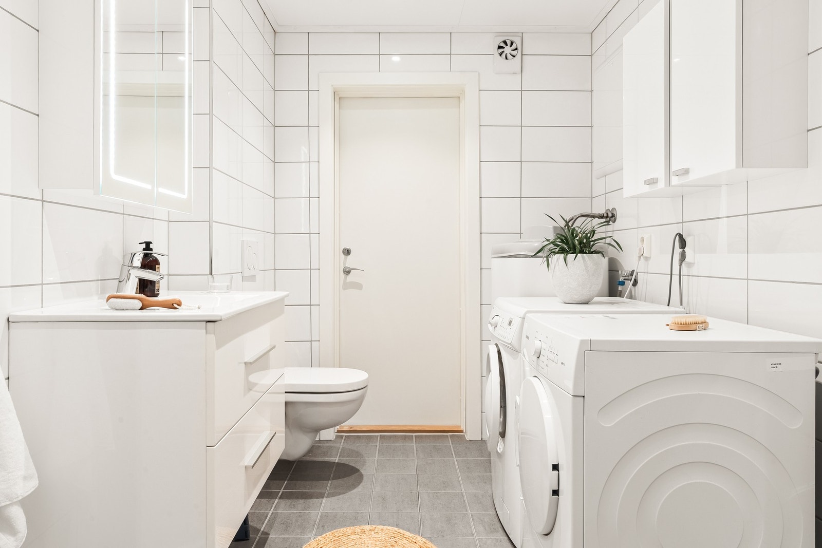 Badet er innredet med veggmontert toalett, skuffeseksjon med overliggende servant, dusjhjørne og opplegg for vaskemaskin. Det er ventilasjon med el-vifte. Galleribilde