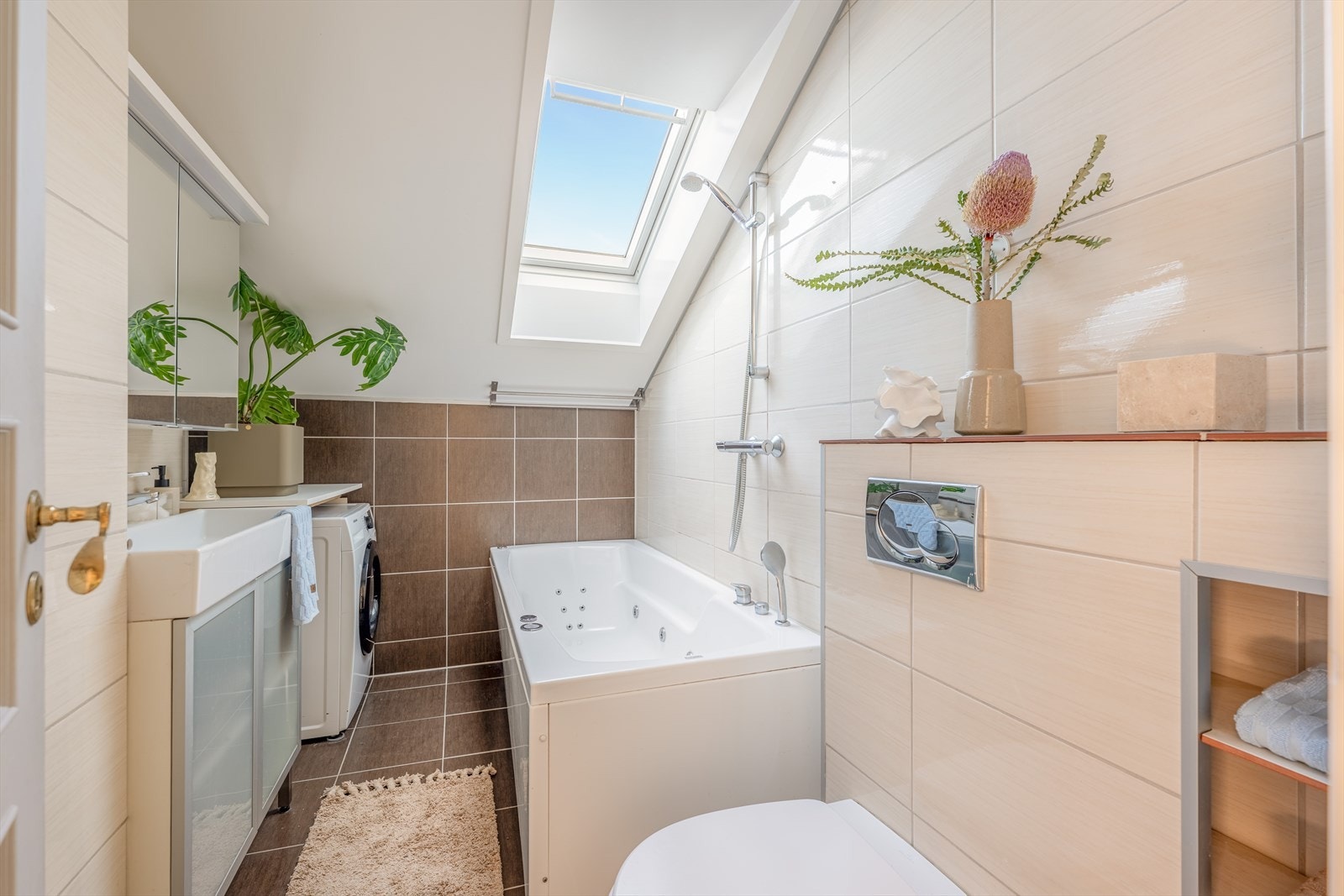 Flislagt bad med boblebadekar, vegghengt toalett, servant og opplegg for vaskemaskin. Galleribilde