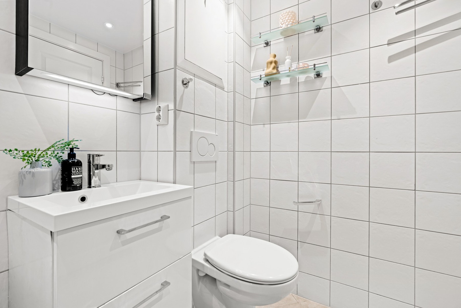 Baderomsinnredningen er moderne og består av et servantmøbel med hvite skuffefronter og en heldekkende servant. Over servanten er det montert et speilskap med integrert belysning. Galleribilde