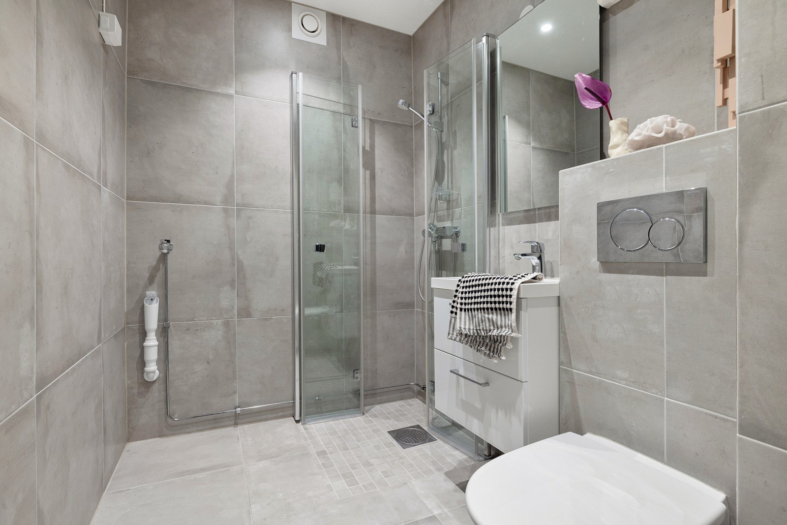 Flislagt bad med varmekabler, avtrekk, speil med belysning, downlights, opplegg for vaskemaskin, servant med innredning, dusj hjørne med innfellbare glassdører, vegghengt toalett. Galleribilde