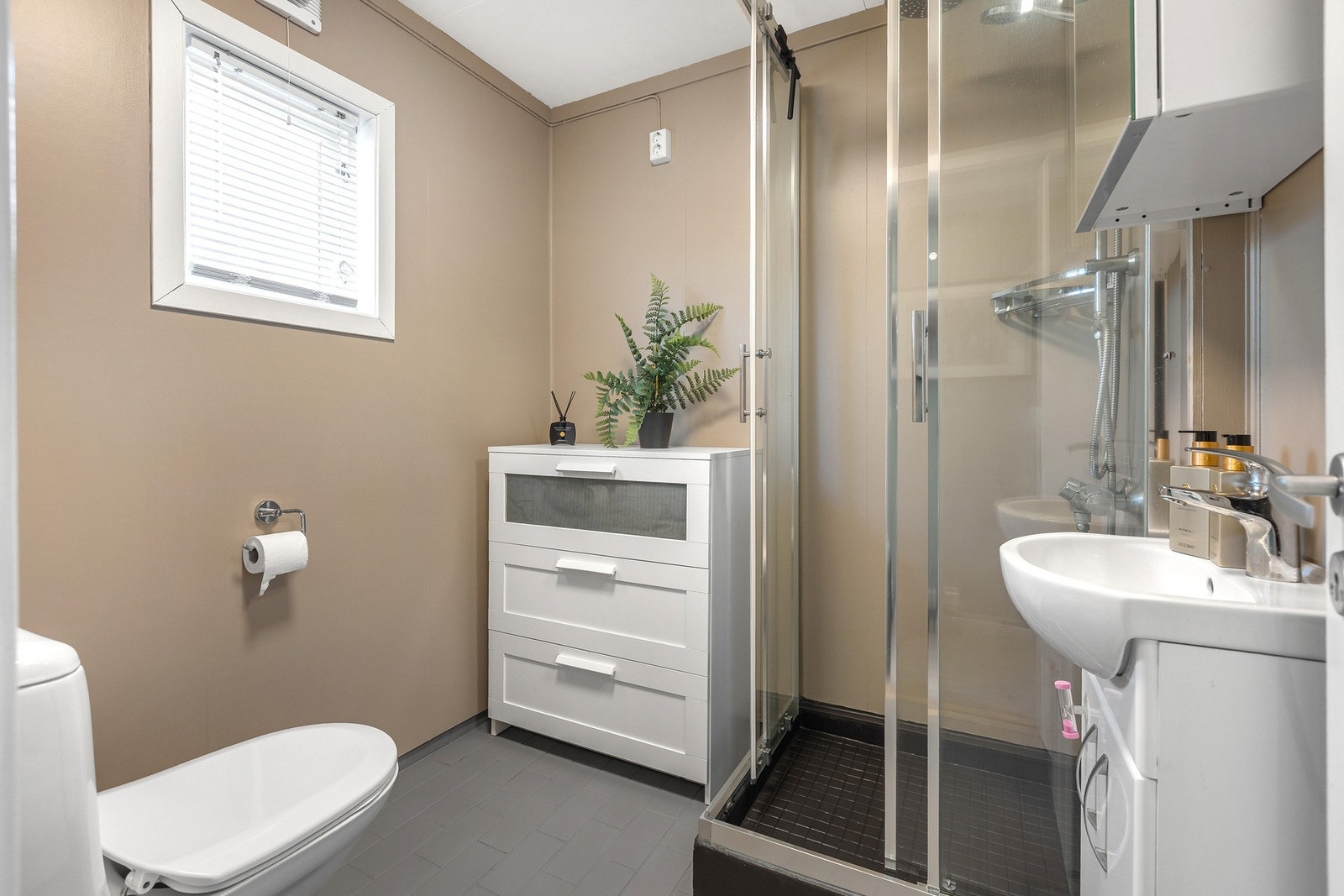 Badet, som ligger i 1.etasje, har eldre standard og har behov for oppgradering til dagens standard. Eldre varmekabler over malte fliser og baderomsplater på vegg. Nyere innredning og toalett. Fast dusjkabinett. Galleribilde