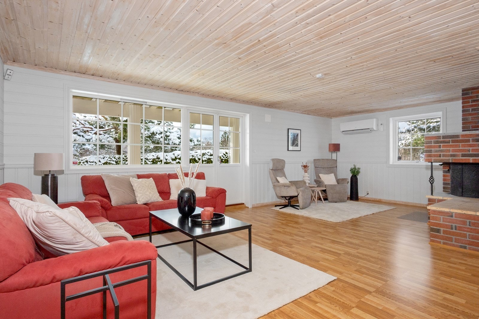 Det er også her installert varmepumpe og en peis bekledd med murstein for hygge og ekstra varme. Verandadør fører ut til hagen. Galleribilde