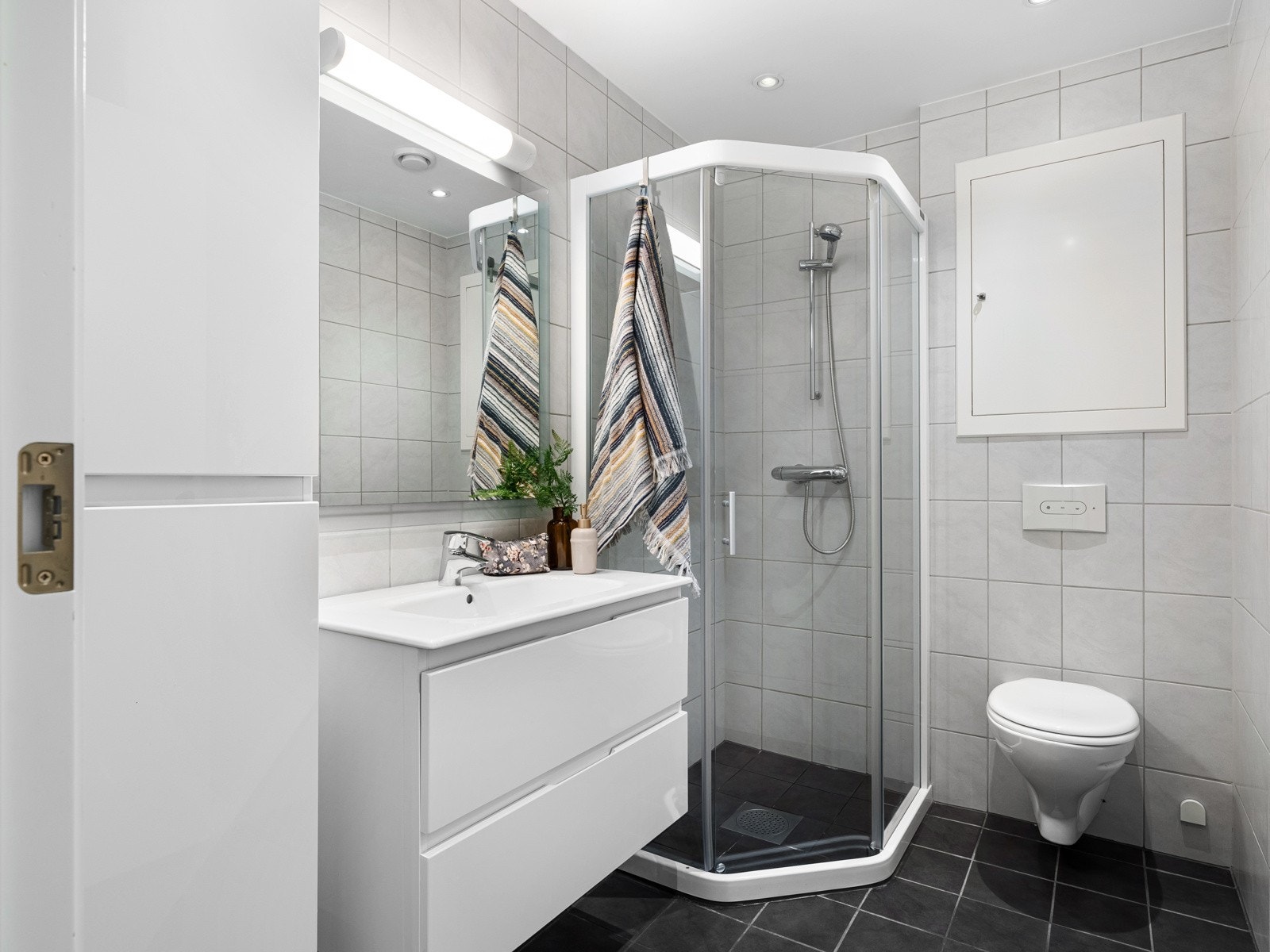 Badet innredet med vegghengt toalett, dusjhjørne, nytt vegghengt skap, ny baderomsseksjon med vask og skuffer for oppbevaring, speil, samt opplegg for vaskemaskin. Galleribilde