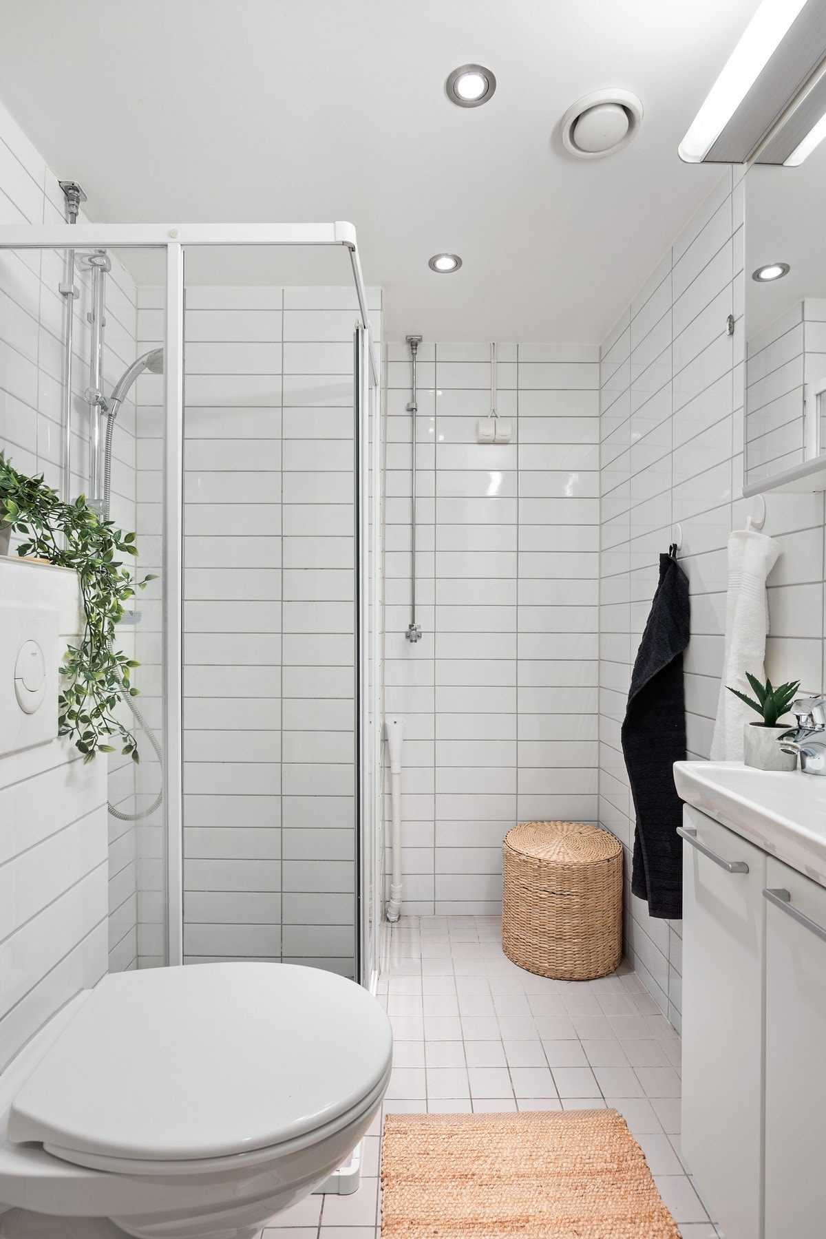 Flislagt baderom med vegghengt wc, dusjhjørne, servantskap med overhengende speilskap og belysning. Galleribilde