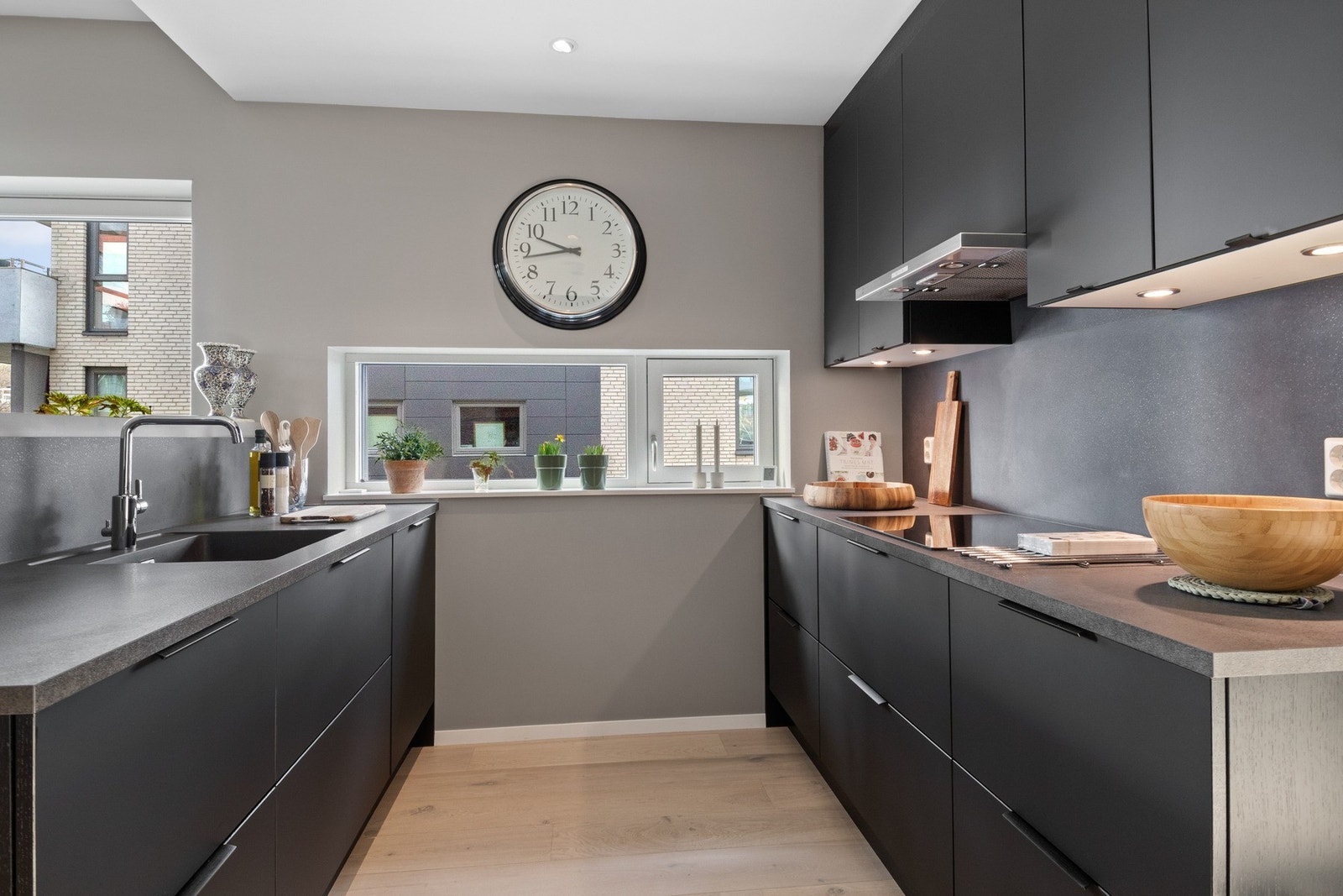 Skap og skuffer har mørkegrå fronter, benkeplatene er i steinimitert laminat og veggene bak har plater som harmonerer godt. Galleribilde