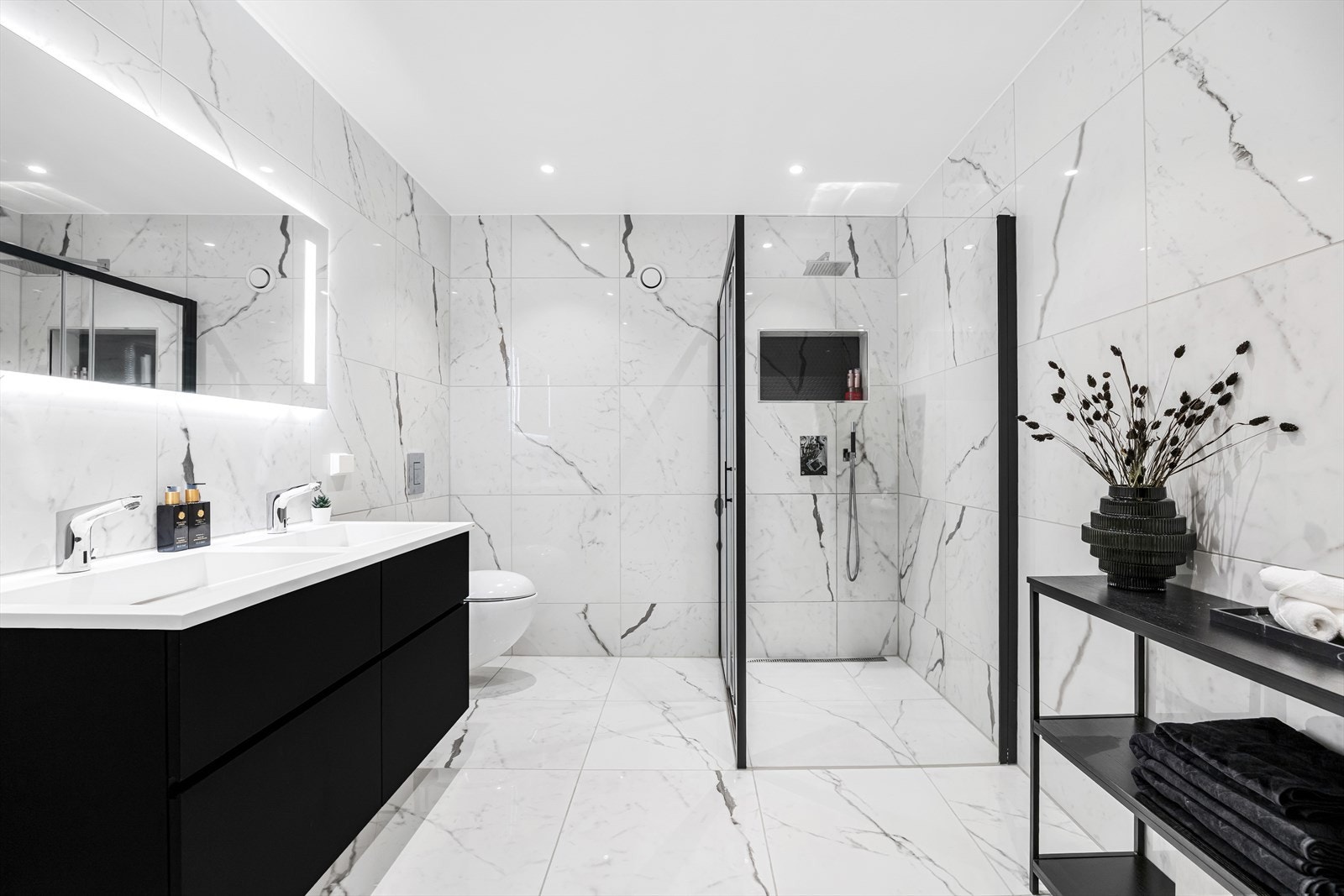 Stort og delikat flislagt masterbad med dobbel servant og vegghengt wc. Stor dusjsone og mulighet for badekar. Innebygget dusjarmatur fra Tapwell. Galleribilde