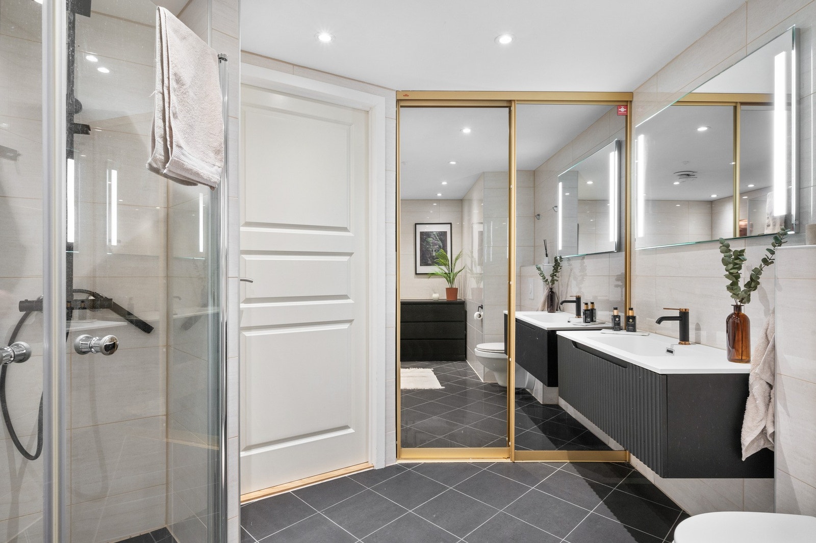 Rommet er innredet med et vegghengt toalett, en helstøpt servant med tilhørende skuffer med profilerte fronter, samt dusjdører i klart glass Galleribilde