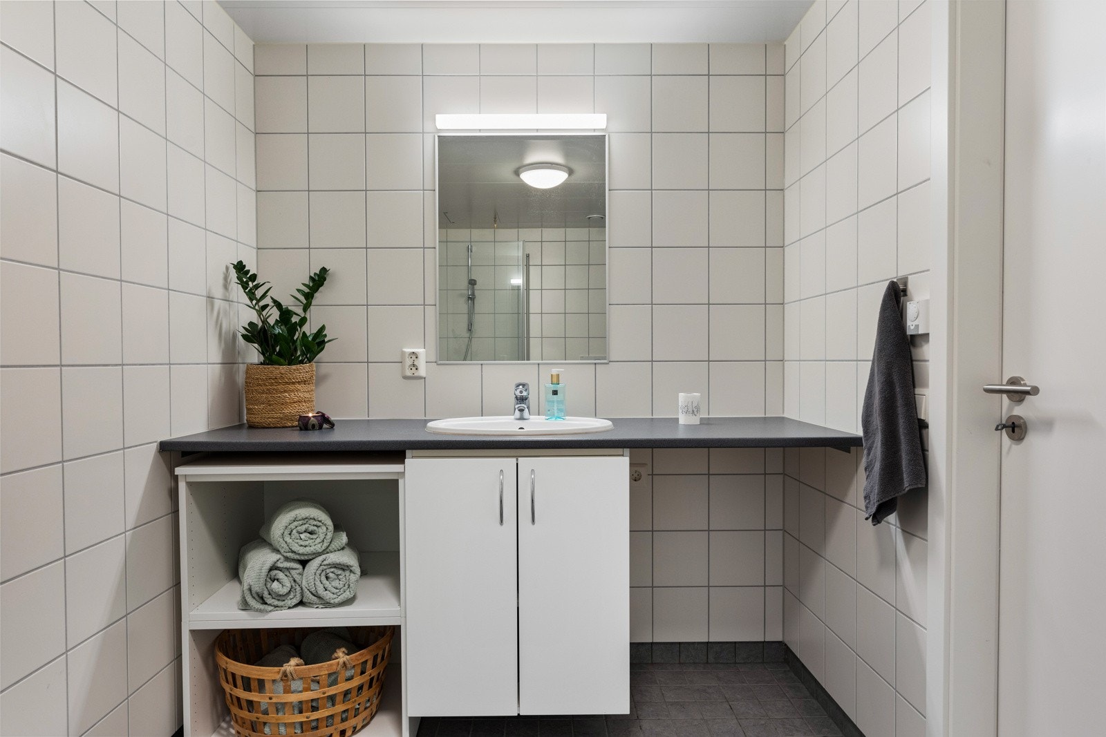 Rommet har opplegg for vaskemaskin, veggmontert toalett, dusjdører i herdet glass og speil med overliggende belysning. Galleribilde