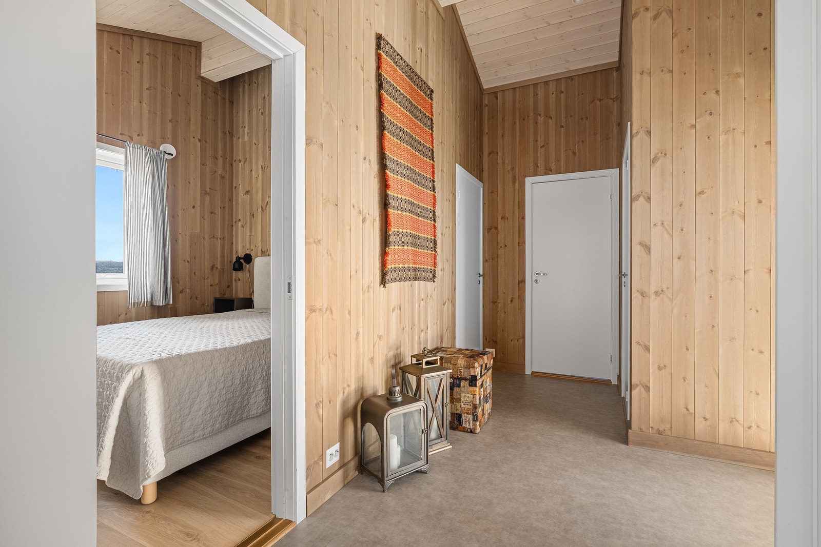 Lyst soverom med vindu, adskilt fra gang med trepanel og flere dører. Galleribilde