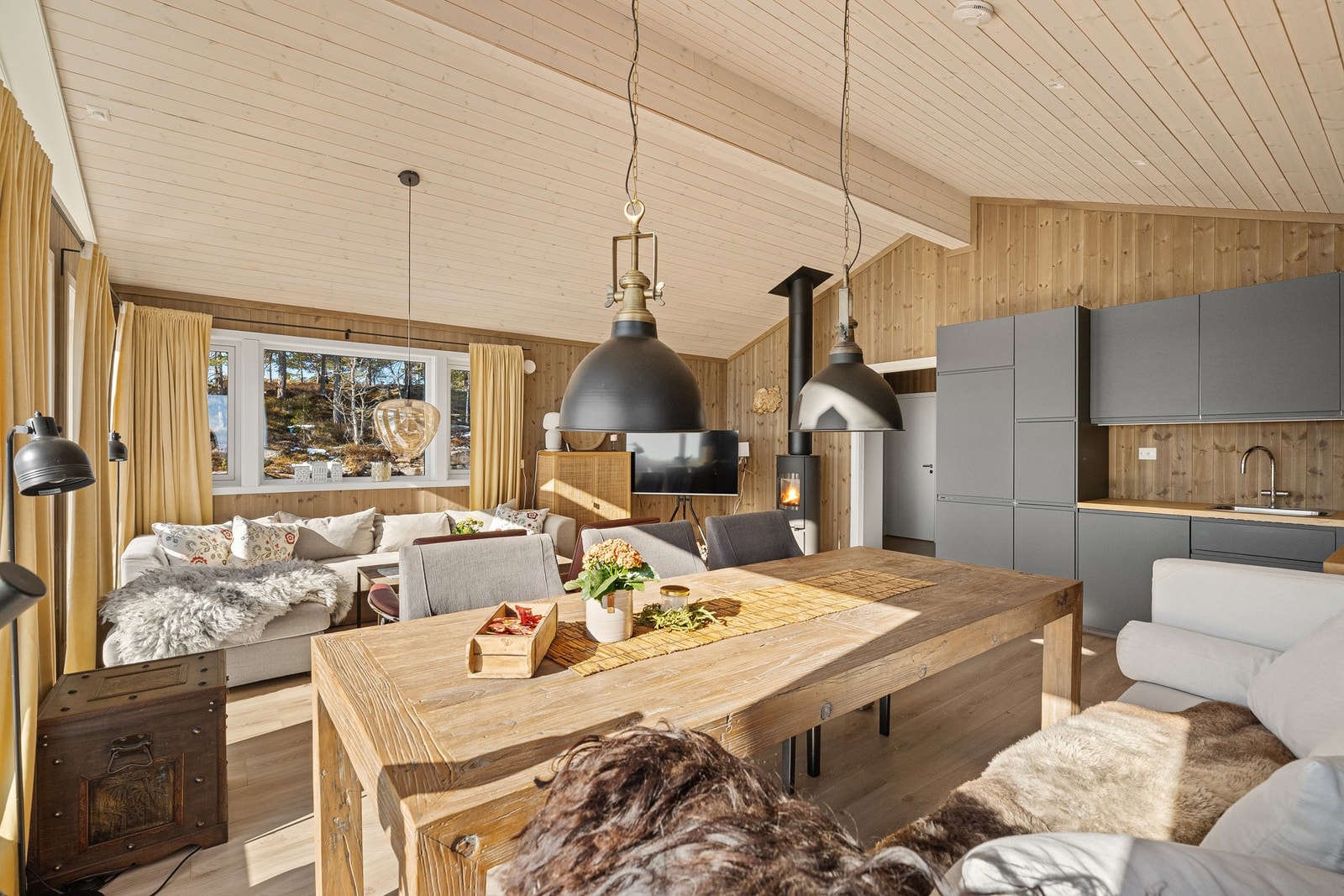 Åpen stue med spisebord, kjøkken, sofa og store vinduer som gir godt lys. Lys og moderne innredning. Galleribilde