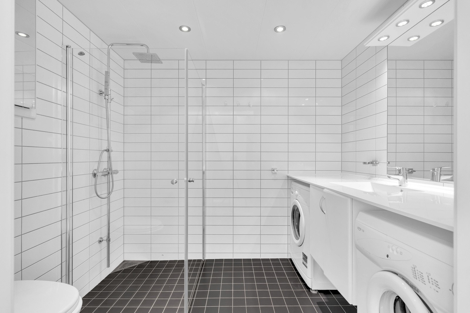 Pent flislagt baderom med elektriske varmekabler og downlights. Rommet har innredning med nedfelt servant, veggmontert toalett, dusjdører og opplegg for vaskemaskin. Det er mekanisk avtrekk. Galleribilde