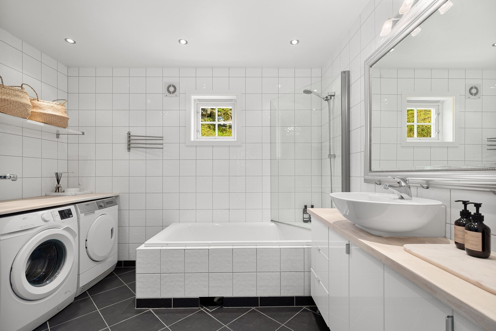 Flislagt baderom med badekar og opplegg for vaskemaskin og tørketrommel. Galleribilde