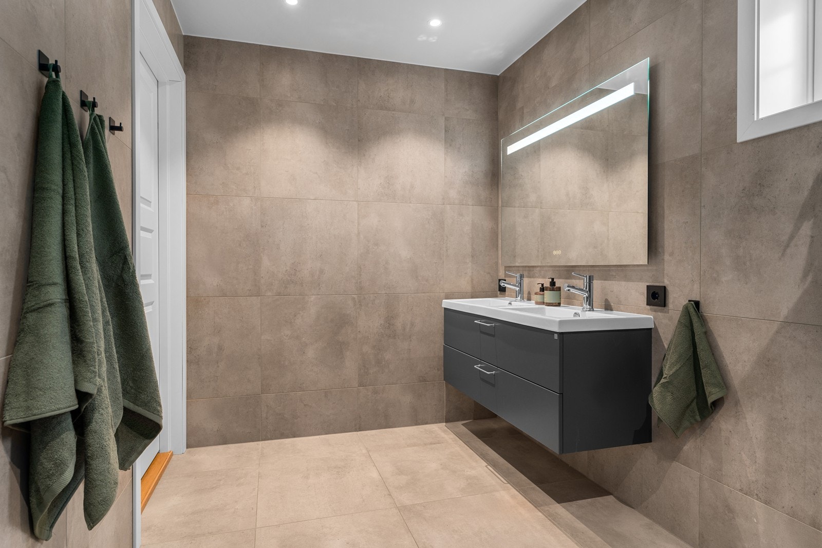 Det andre badet er kombinert bad og vaskerom. Badet er romslig med smarte løsninger. Det er montert servant med ett-greps servantbatteri som er nedfelt i den store benkeplaten med underliggende benkeskap. Galleribilde