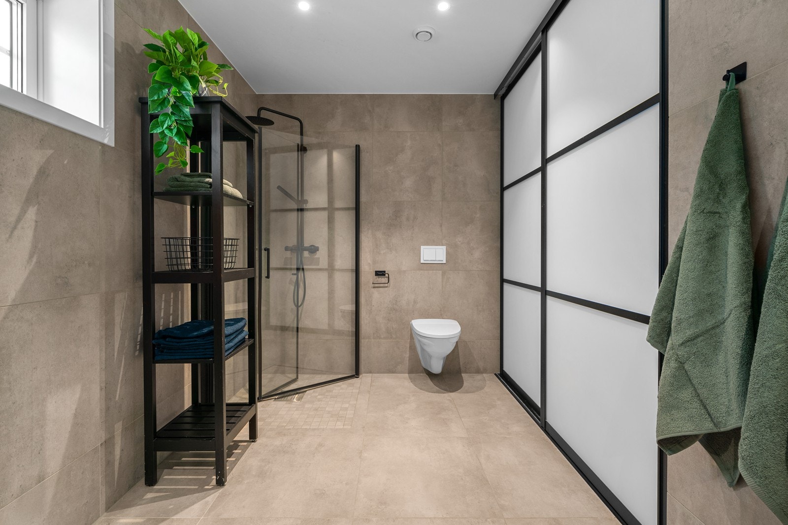 I det ene hjørnet er det veggmonterte svingbare dusjvegger av herdet glass. Skjult bad to skyvedører finner man vaskesøyle med uttak for både vaskemaskin og tørketrommel. Her står også varmtvannsbereder. Galleribilde