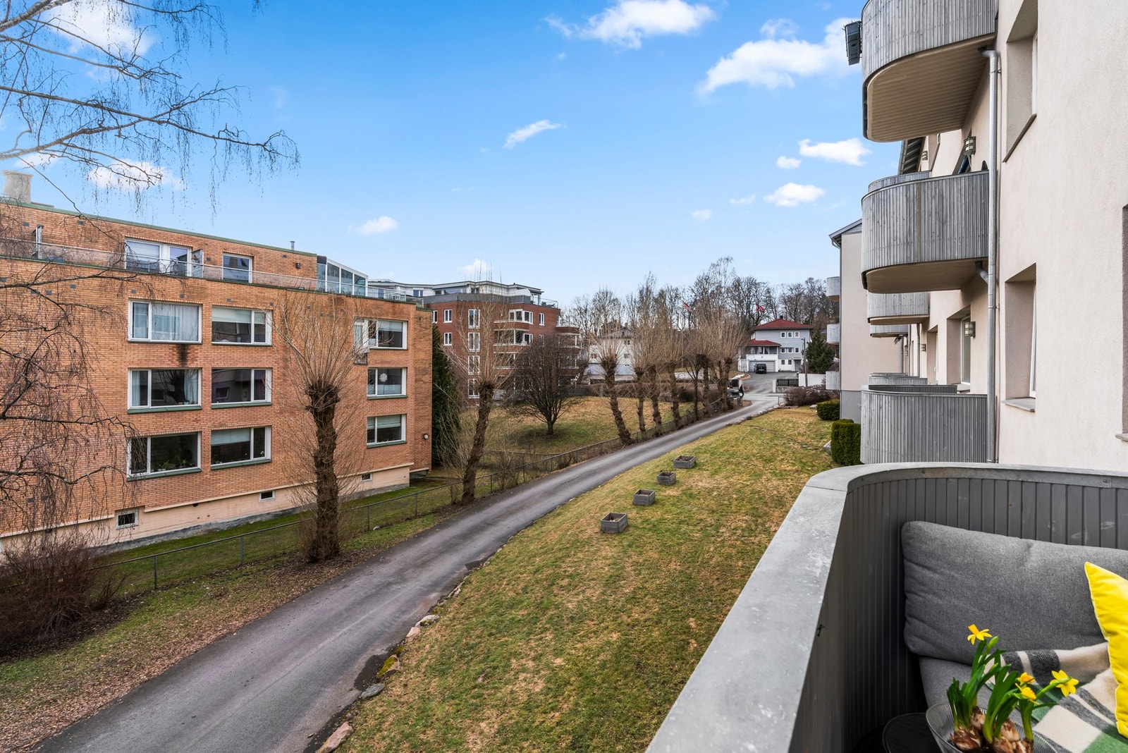 Høy første etasje, gjør at balkongen ligger godt over bakkeplan. Grøntområdene foran leiligheten er i ferd med å blomstre, og da er det vakkert her ute Galleribilde