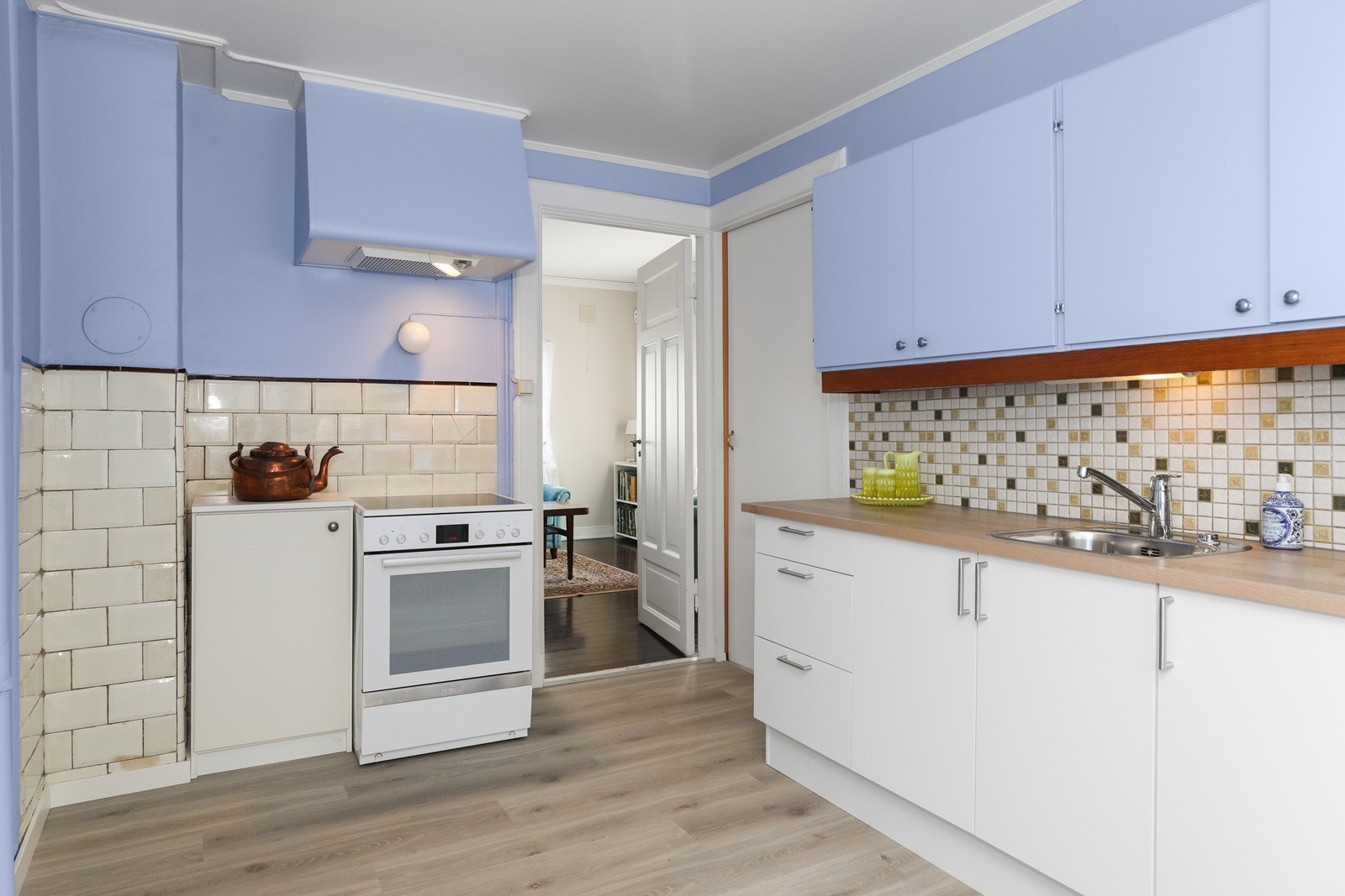 Kjøkkeninnredning med slette fronter og laminat benkeplate. Denne er ny i 2025 mens overskap og lite benkeskap i hjørne er av eldre dato. Det er lagt fliser på vegg over benken Galleribilde