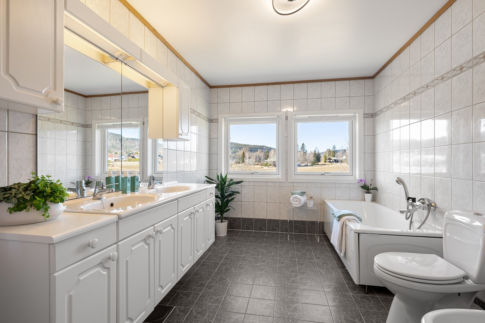 Romslig og pent bad med flislagte overflater. Badet er utstyrt med wc, bidé, badekar, elektrisk håndkletørker og dobbelservant i innredning. Galleribilde