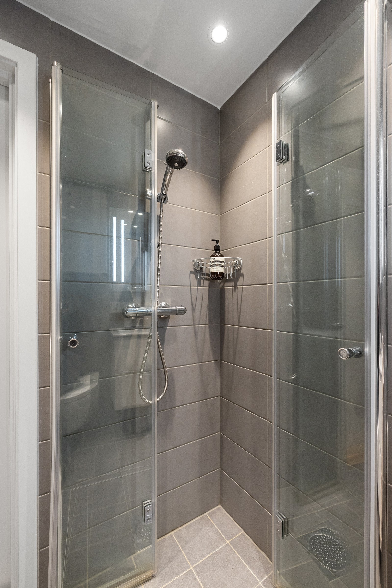 Innredningen består av glatte fronter, heldekkende servant og speil over med tilhørende belysning. Dusjhjørne med glassvegger og vegghengt toalet Galleribilde