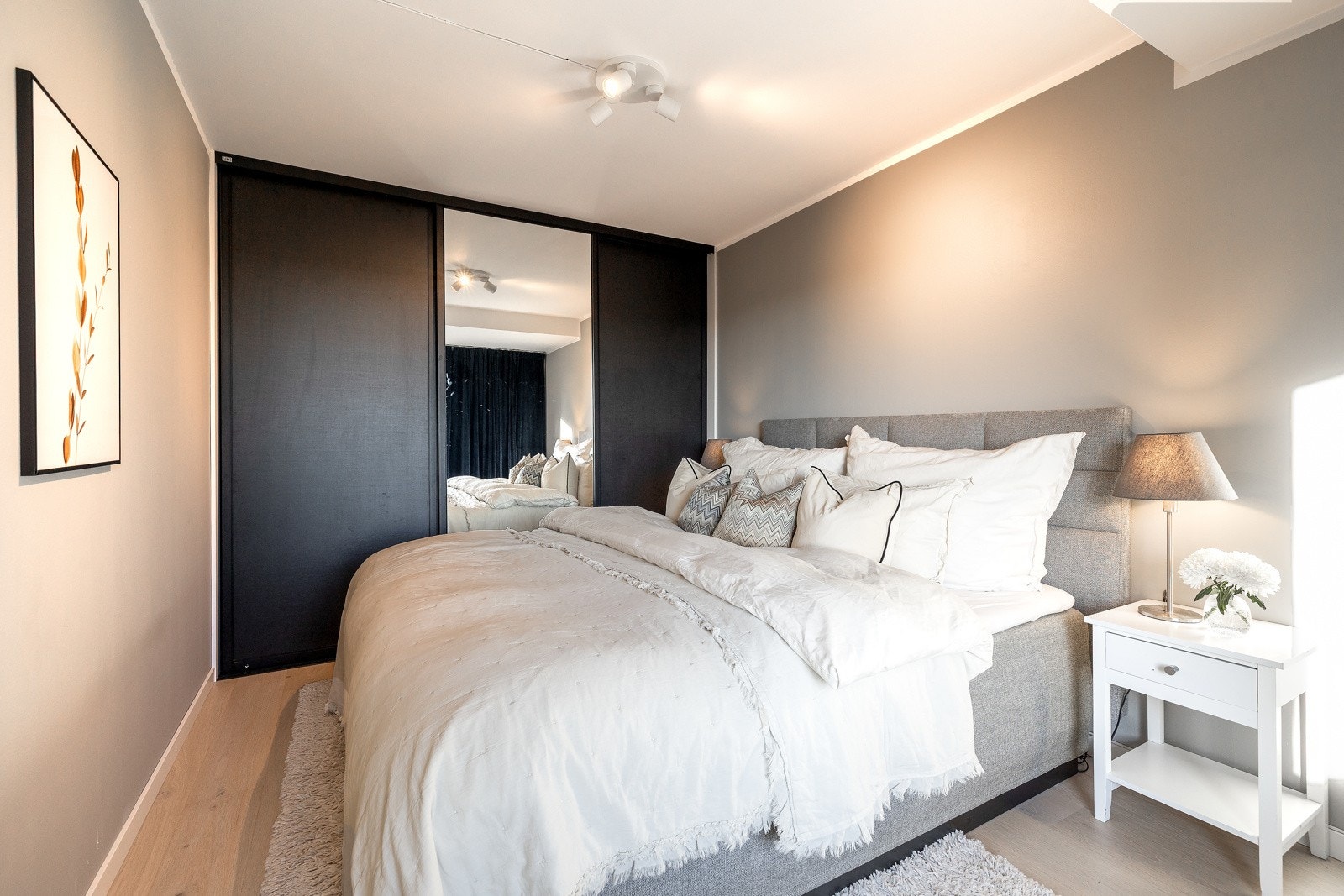 Klær kan ryddes pent vekk i en skyvedørsgarderobe med to mørke fronter og en speilfront Galleribilde