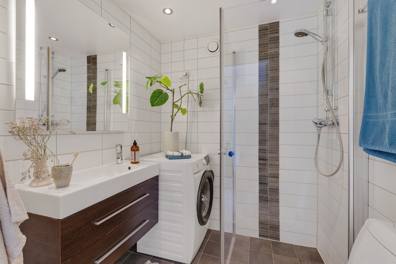 Badet inneholder vegghengt baderomsinnredning med skuffer og heldekkende servant, speil med belysning, toalett og dusjhjørne med innfellbare dører i glass. Galleribilde