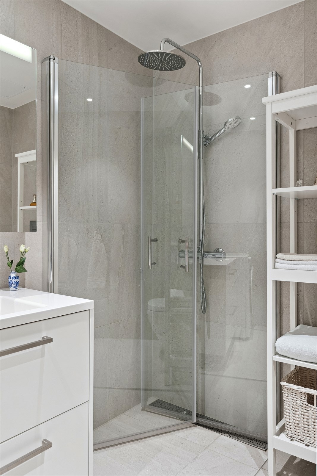 Badet er innredet med et hvitt servantskap med to store skuffer, speilskap med LED-lys, vegghengt toalett og dusjhjørne med glassdører og regnfalls- og hånddusj. Galleribilde