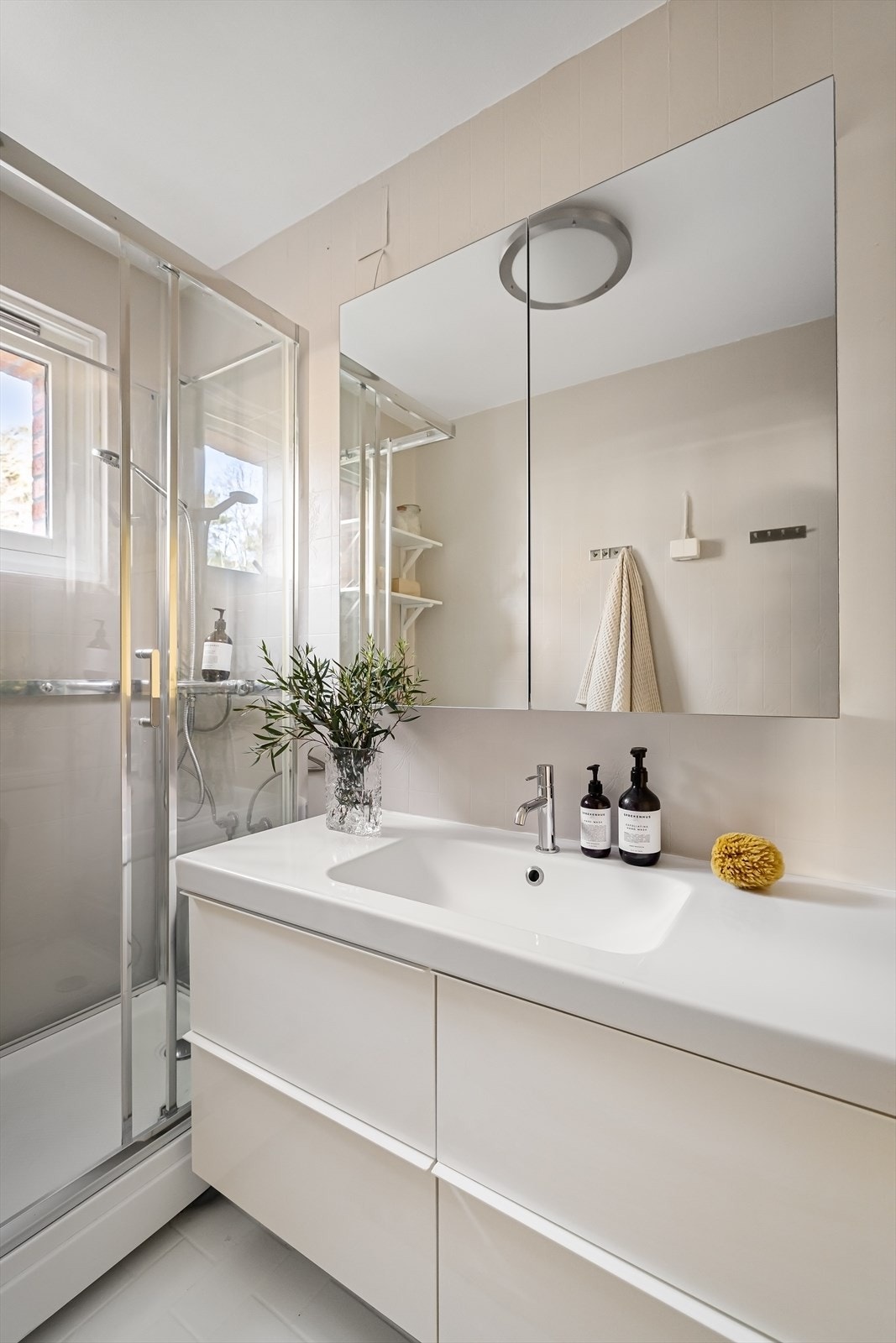 Badet er utstyrt med gulvstående toalett, dusjkabinett med skyvedører, heldekkende servant med dobbel skuffeinnredning under og speilskap over Galleribilde