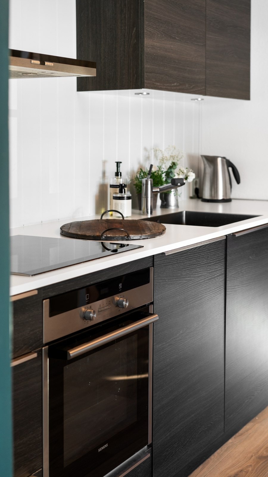 Kjøkkeninnredningen er moderne utført med mørke, glatte fronter og hvit laminert benkeplate med kjøkkenkum. Galleribilde