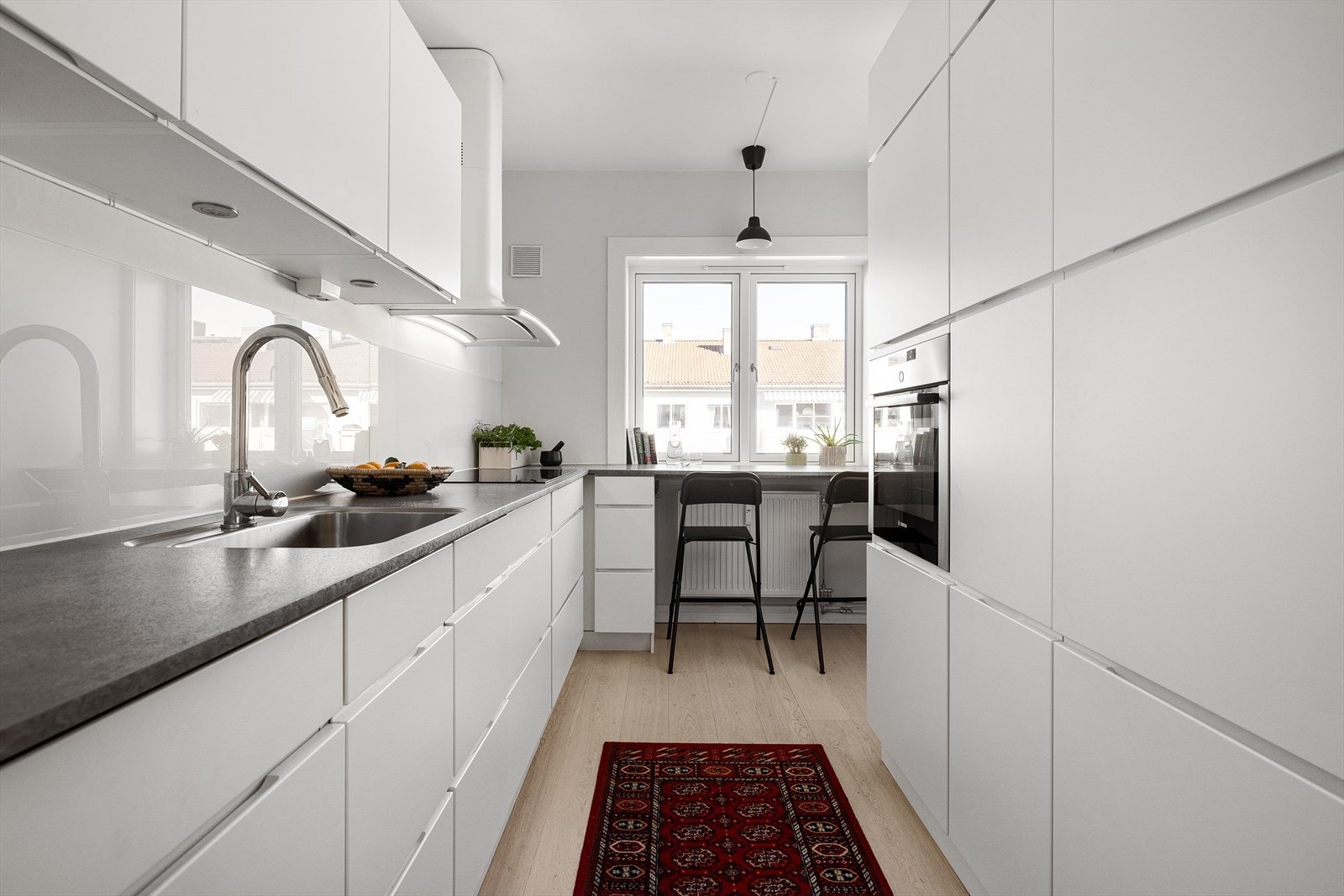 Lekkert velutstyrt kjøkken med gode arbeidsflater, integrerte hvitevarer og en koselig frokost-benk Galleribilde