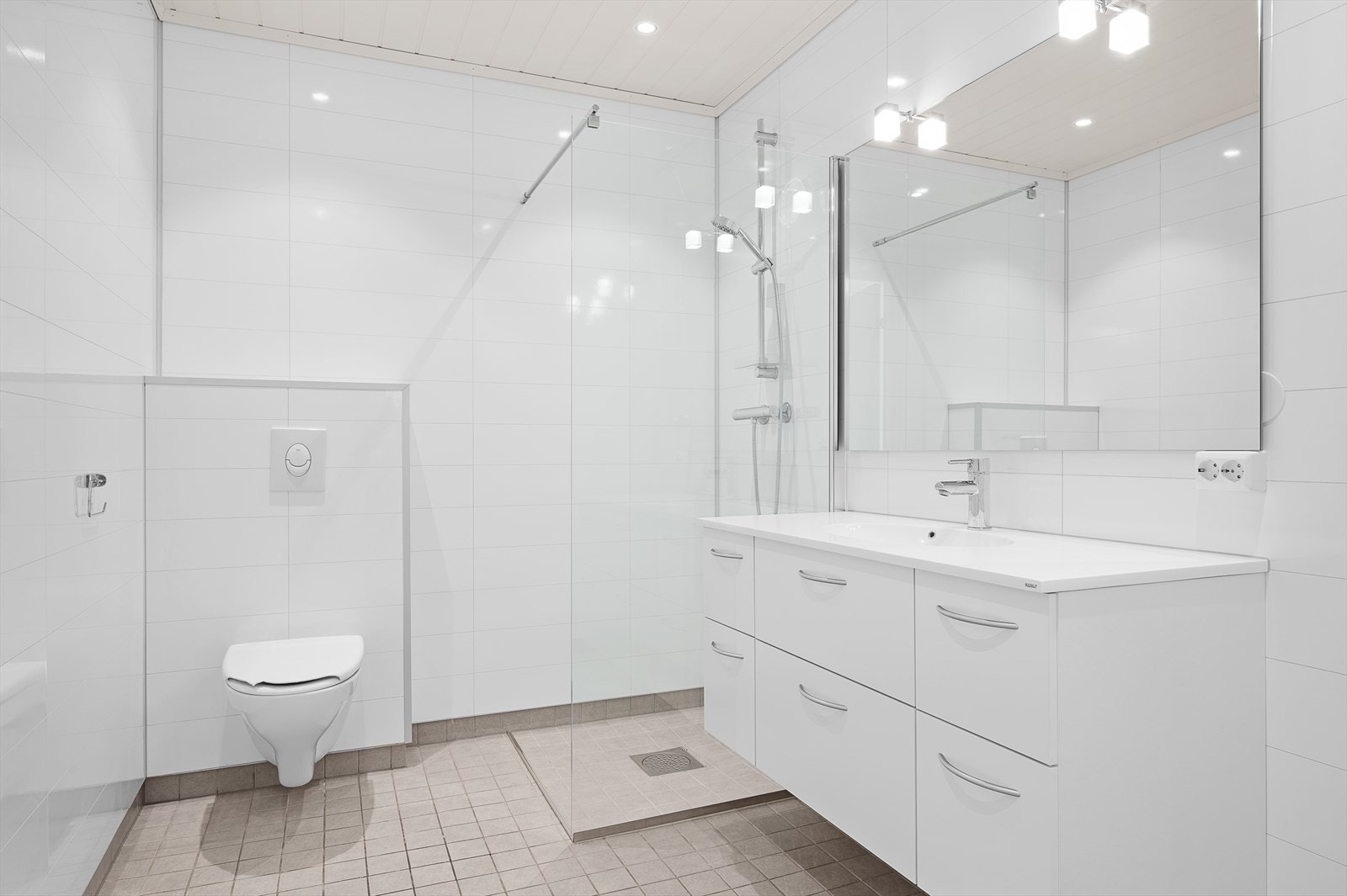 Pent bad med flislagt gulv (varmekabler) og våtromsplater på vegg. MDF himling med downlights. Dusjhjørne, vegghengt toalett og servant i pen innredning. Opplegg til vaskemaskin. Galleribilde