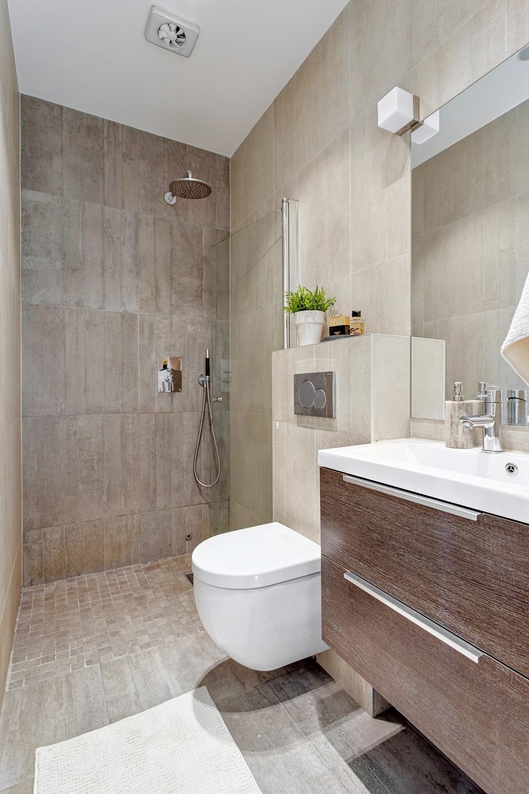 Flislagt bad med vegghengt toalett, dusj, servant med ett-greps blandebatteri og servantskap Galleribilde