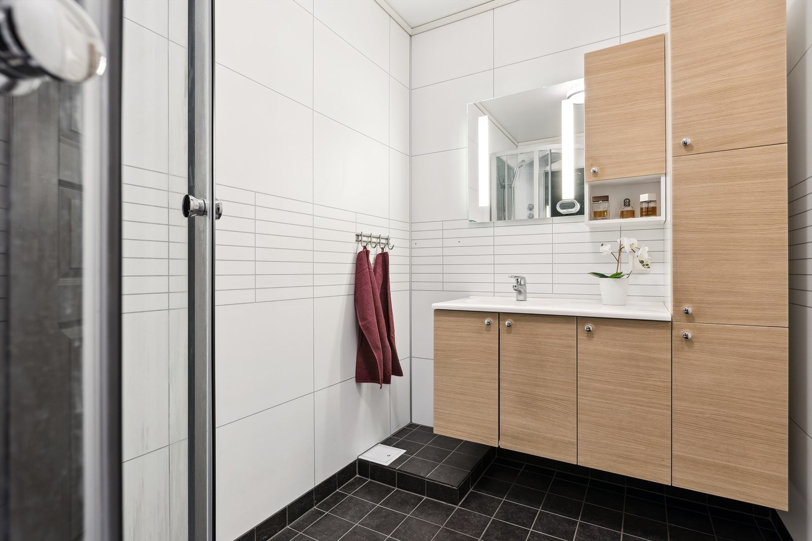 Badet er flislagt på gulv og vegger, samt utstyrt med servantskap og speil med integrert belysning. Galleribilde