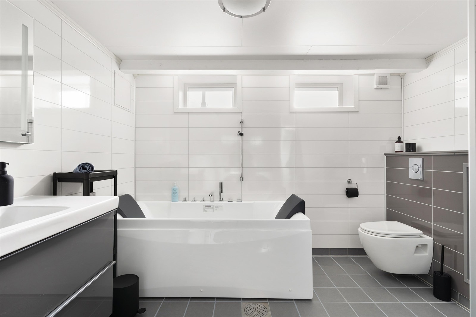 Videre er badet innredet med enkeltservant, speil med lys, badekar og vegghengt toalett. Det er lagt benkeplate over vaskemaskin som gir en flott arbeidsflate. Galleribilde