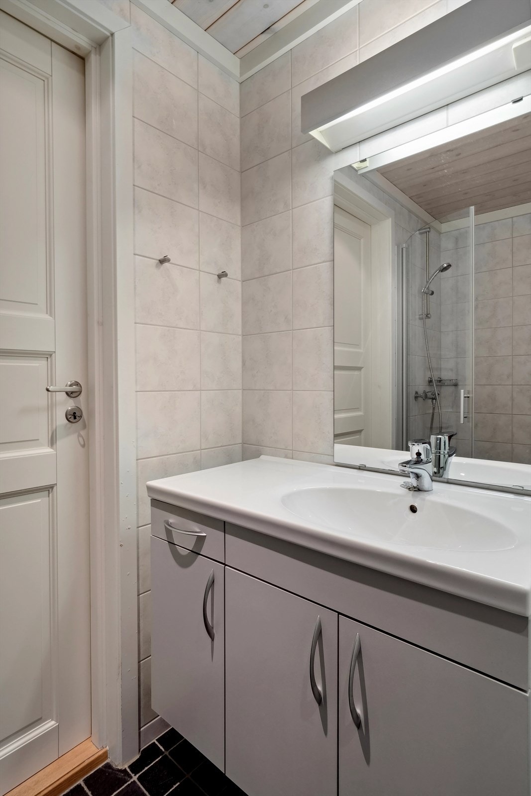 Badet er utstyrt med underskap, speil med tilhørende belysning, dusjvegger og vegghengt wc. Det er plass og opplegg for vaskemaskin. Galleribilde